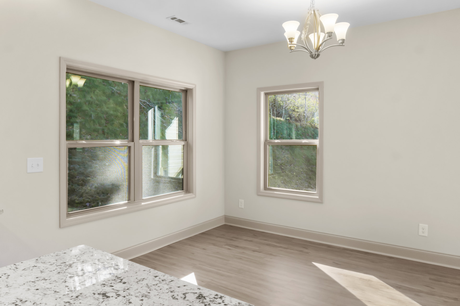 Marble countertop kitchen with large windows overlooking green field and hills, chandelier hanging above, plaster walls, and light switch visible on side wall