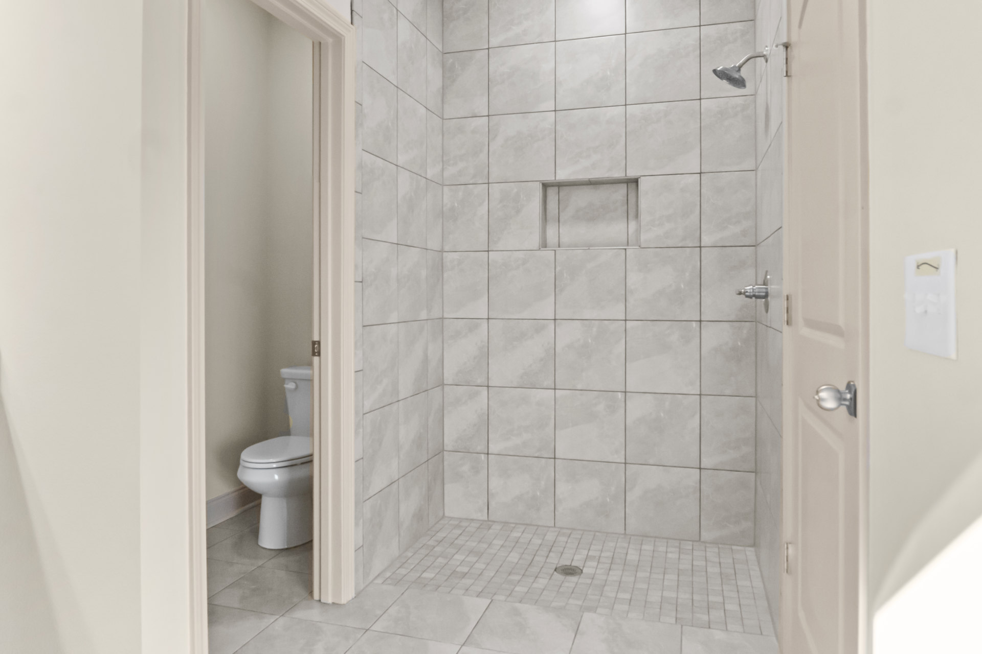 Modern bathroom featuring a white toilet with closed lid, glass-enclosed shower with tile floor, light-colored walls, and chrome fixtures.