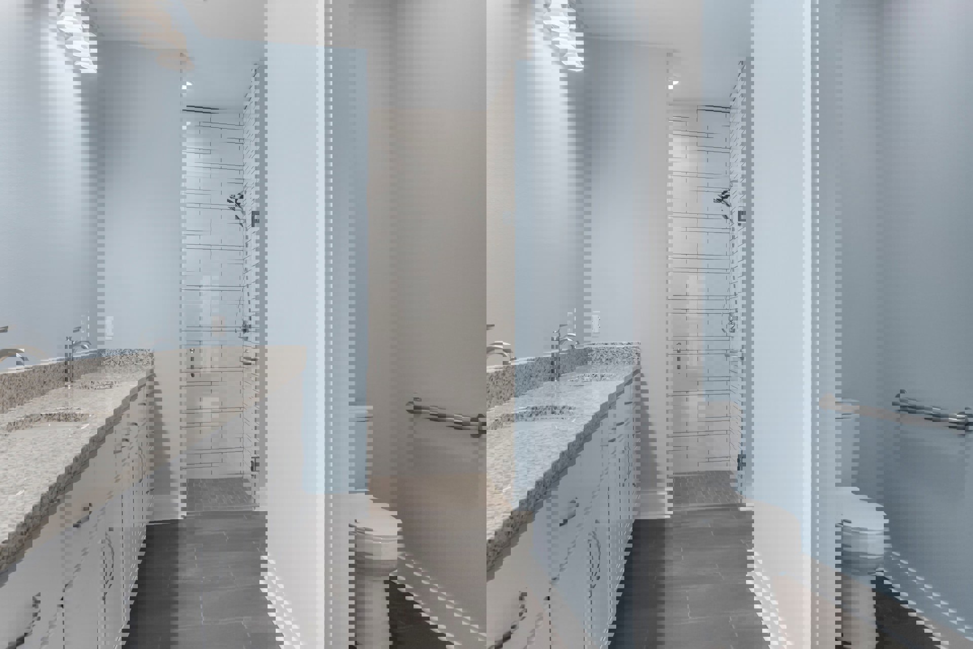 Bathroom with grey tile floor, white cabinets and sinks, glass shower enclosure, chrome fixtures, white toilet, and wall-mounted metal towel bar.