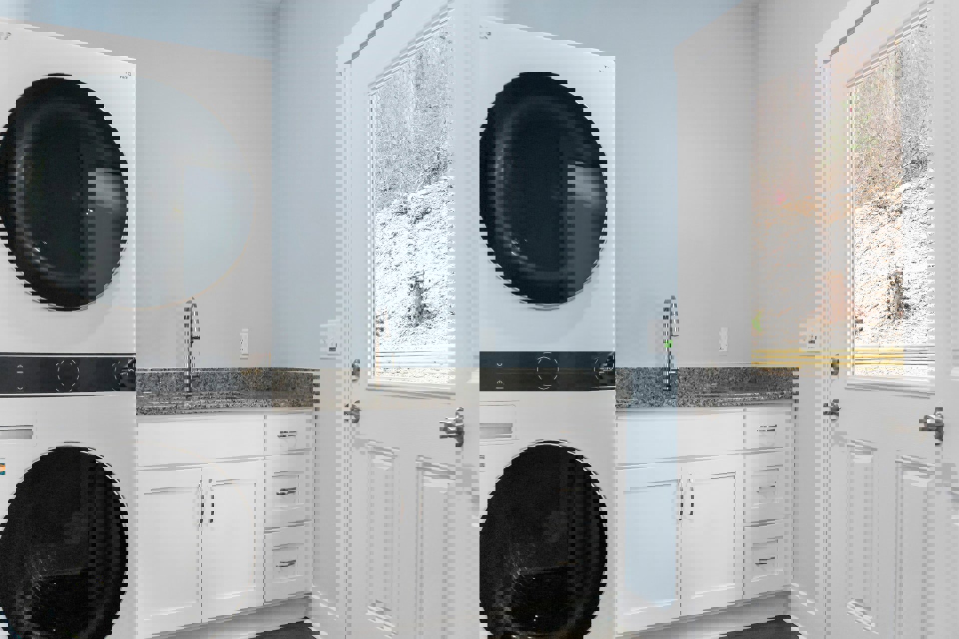 Laundry room with white cabinetry, stainless steel sink, and front-loading washing machine against a light-colored wall