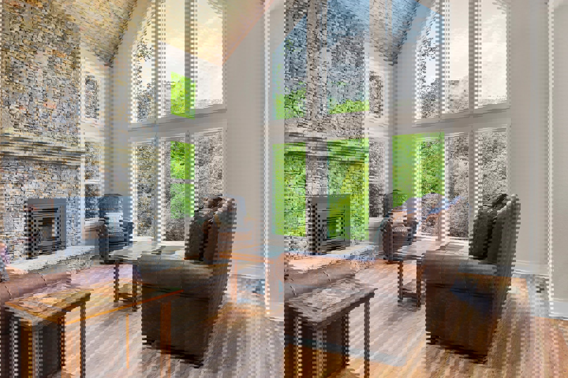 Living room with brown leather couches, wood coffee table, black stove fireplace with glass door, large windows, and neutral walls