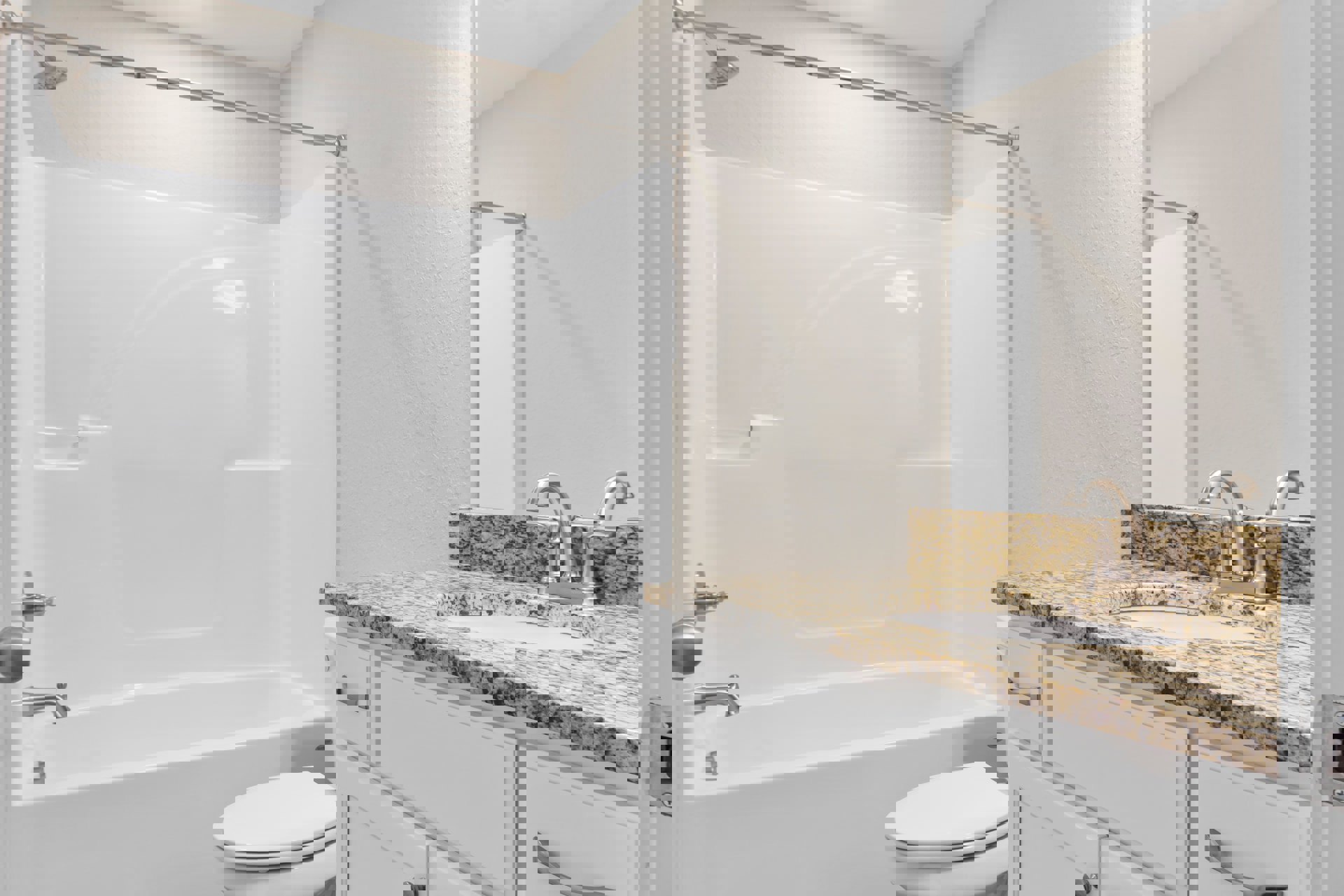 Modern bathroom with white porcelain sink, marble countertop, white toilet, glass-enclosed shower, and light gray tile walls