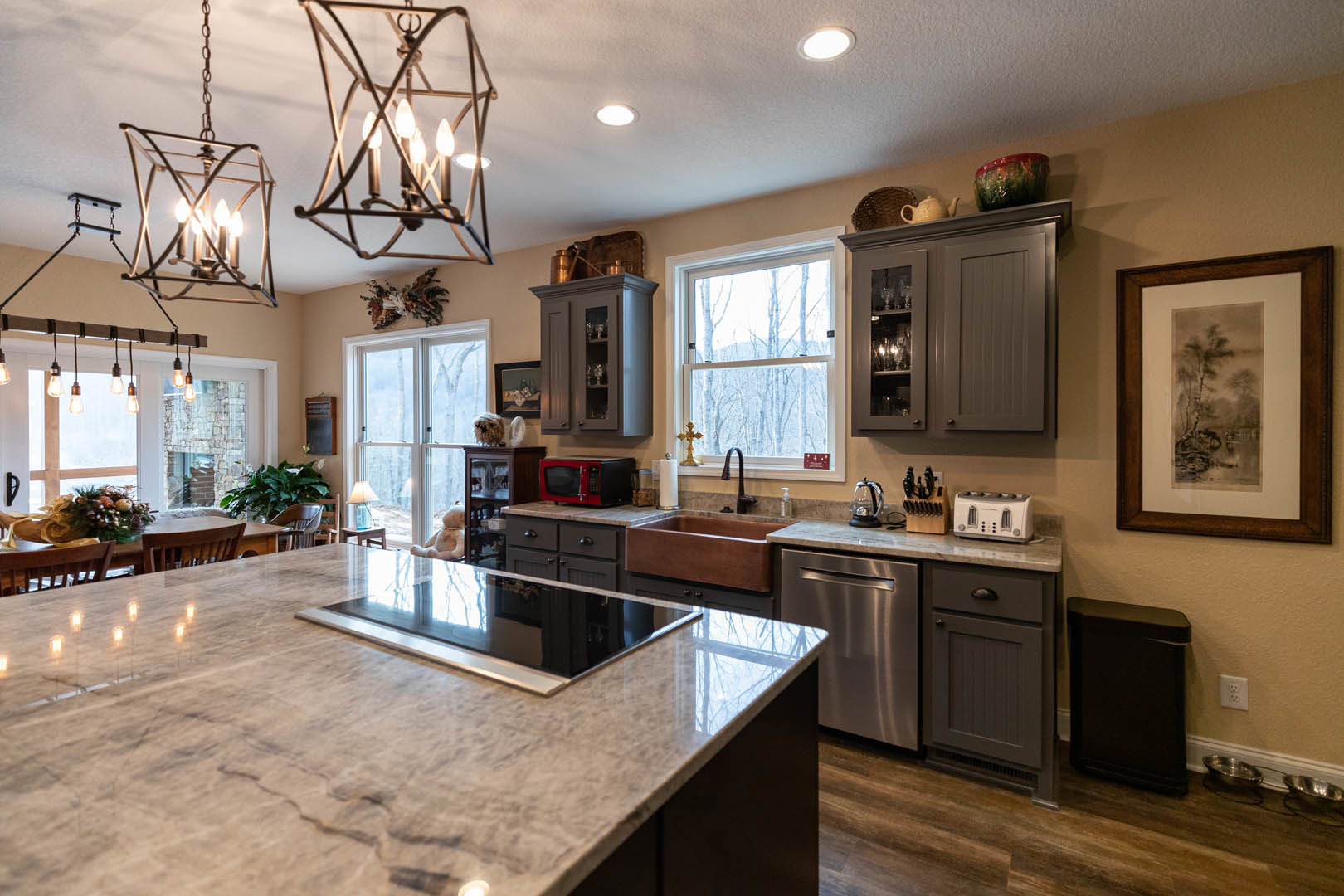 Spacious kitchen featuring a large central island with stone countertop, white cabinetry, stainless steel sink, red microwave oven, framed landscape artwork on the wall, window