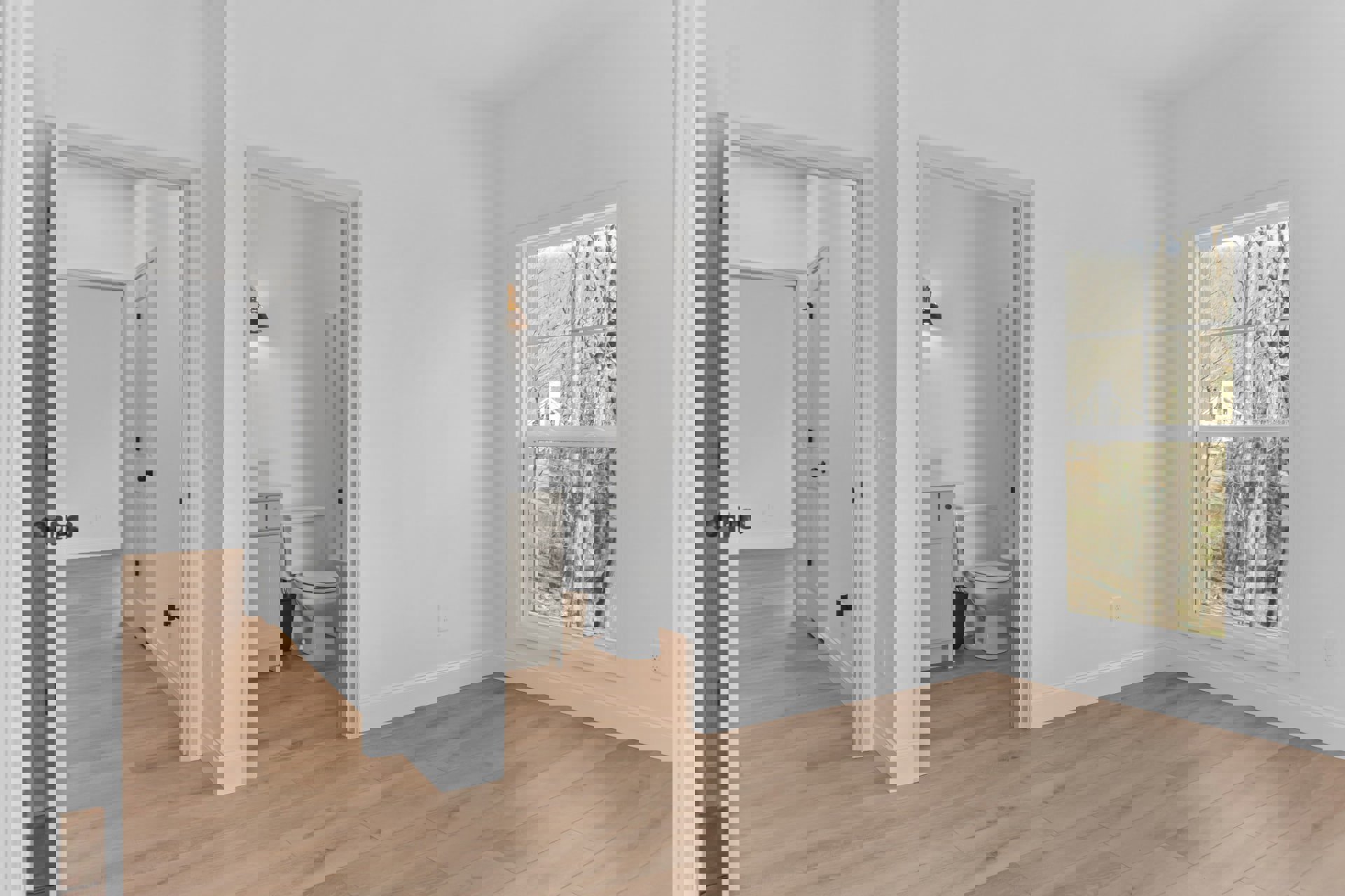 Bathroom with a white toilet, wood laminate flooring, white plaster walls, window showing trees outside, and a modern light fixture