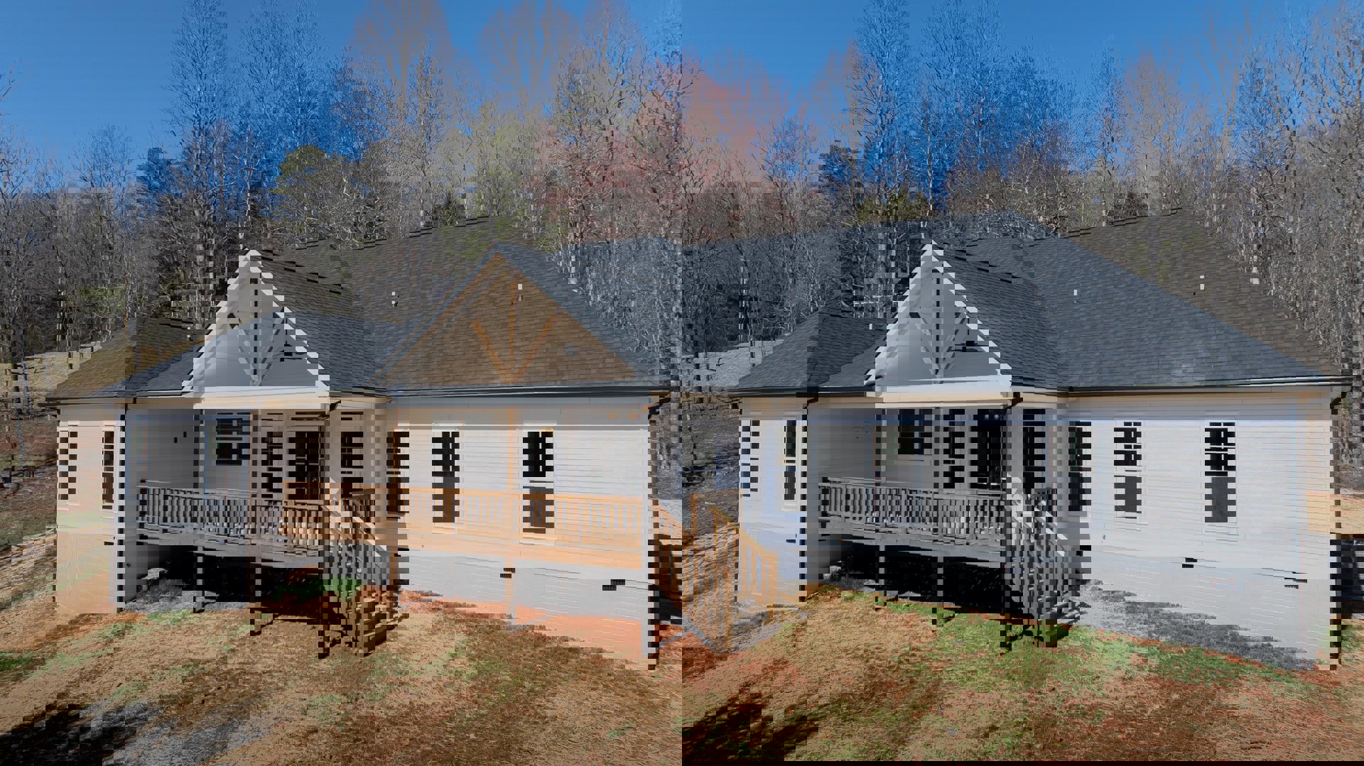 Wooden deck and porch with white-framed windows, square panes, wooden stairs, gray siding, gabled roof, mature trees in background