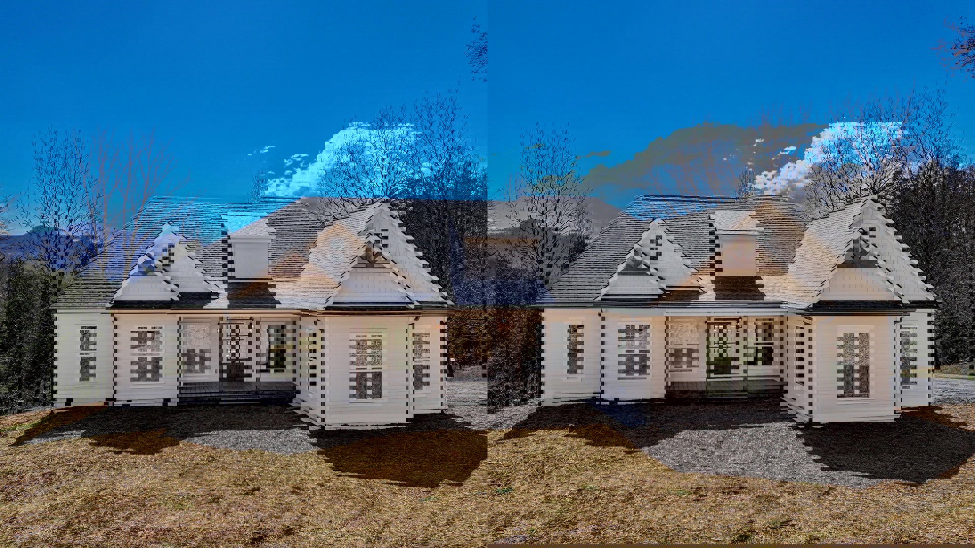 White siding house with double glass doors, multiple square windows, and green grass yard; trees and blue sky in background
