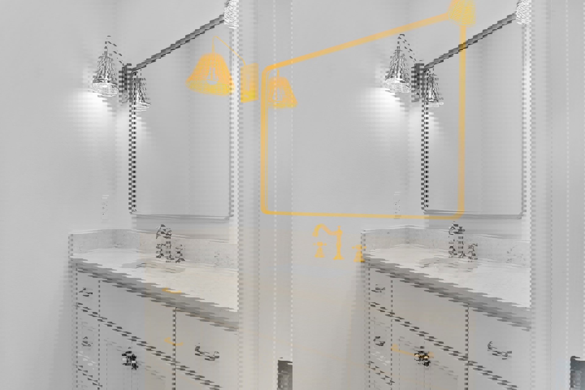 Bathroom vanity with white sink, gold-framed mirror, brass light fixture, wood cabinetry, and metal drawer pulls