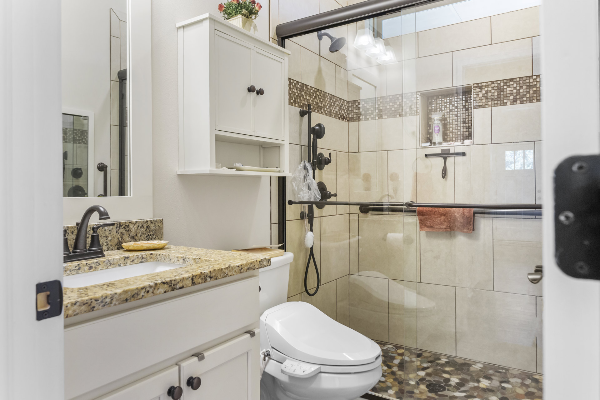 Modern bathroom featuring a glass shower door, white toilet with seat cover, vessel sink on a countertop, small plant in a white pot, tiled floor with drain, and wall-mounted