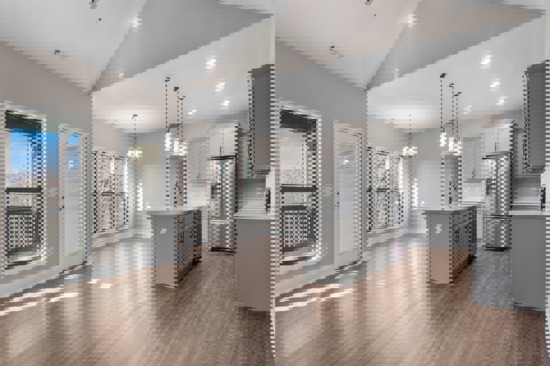 Open kitchen and living room with light wood flooring, white cabinetry, stainless steel refrigerator, large window showing trees and blue sky, modern grey door with frosted glass