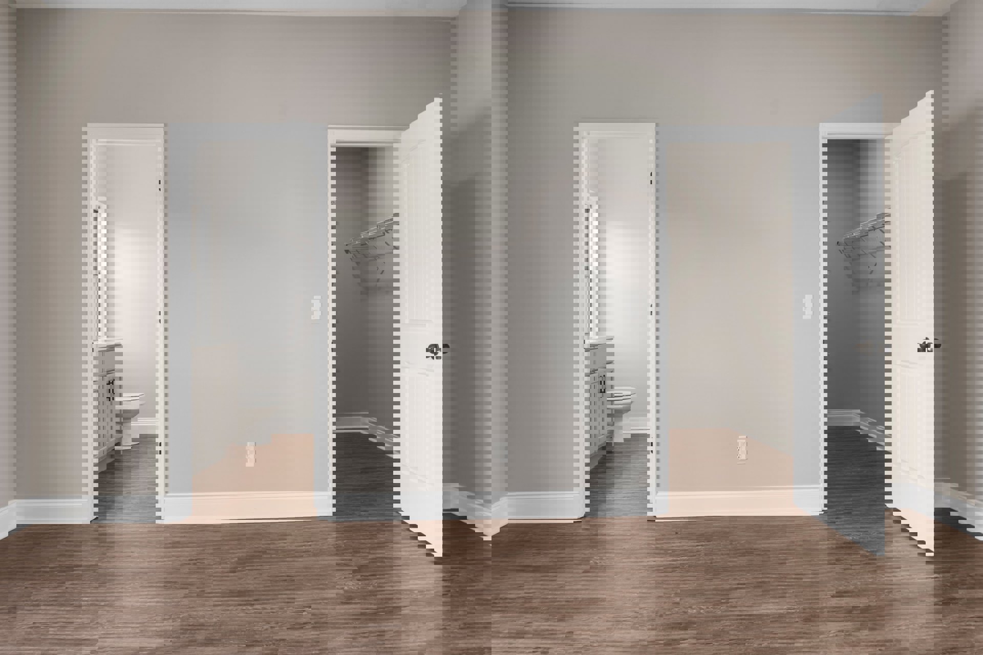 Bathroom with light wood laminate flooring, white toilet and sink, open white door, white plaster walls, and visible electrical outlet on the floor.