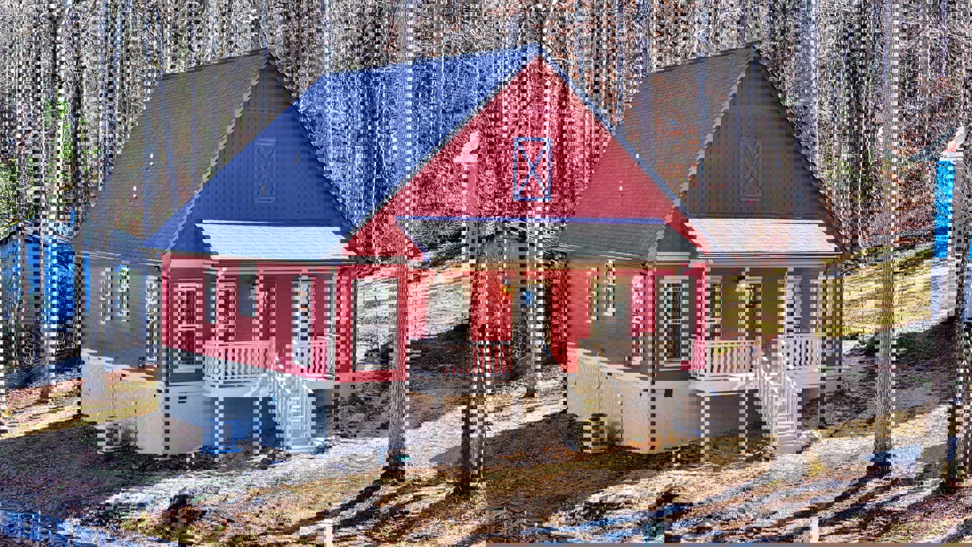 Red clapboard siding house with white-trimmed windows, covered front porch, wooden stairs, blue roof, and surrounding greenery.