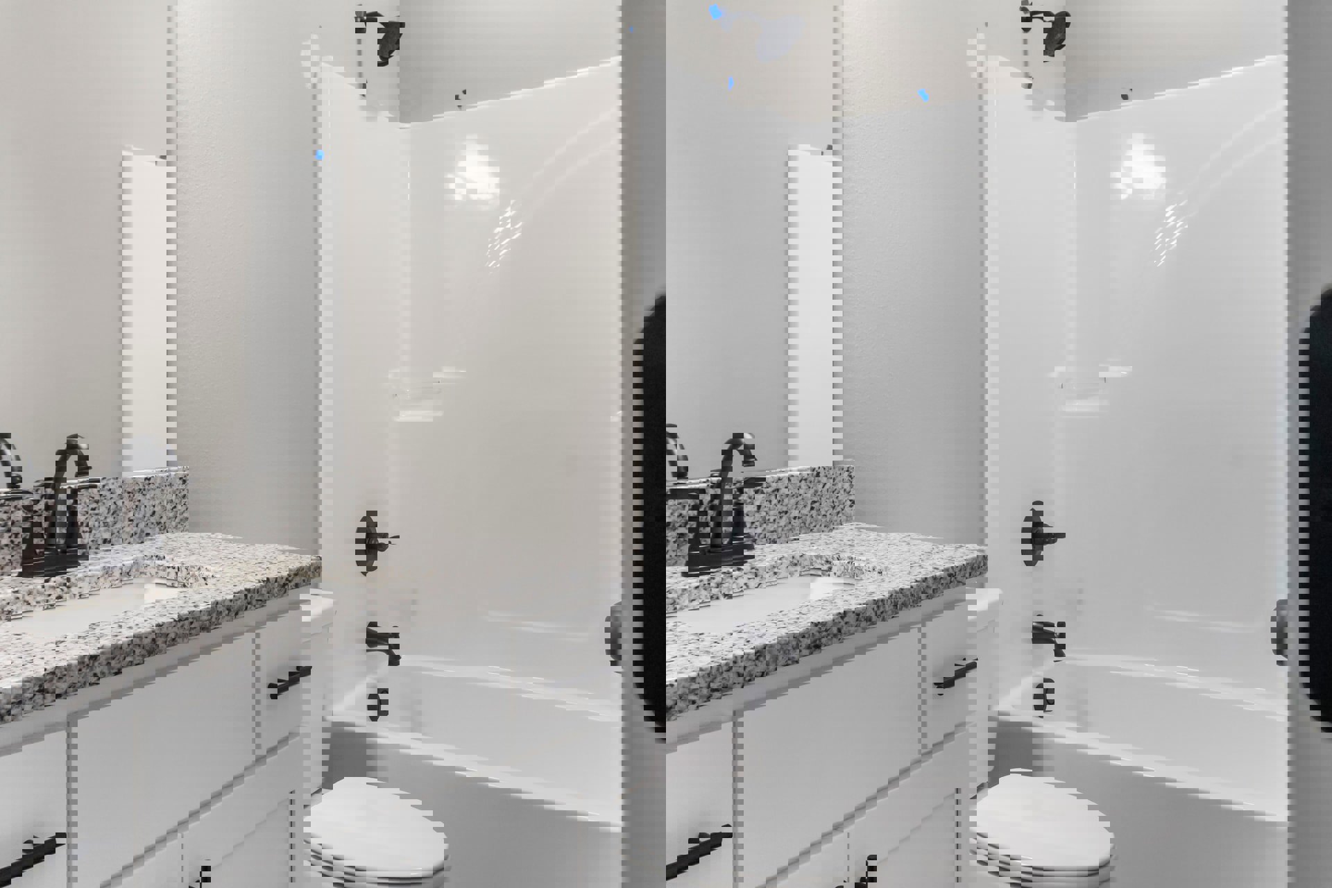 Marble countertop with black faucet, white rectangular sink, white toilet, glass-enclosed shower, light tile flooring, and neutral wall finishes