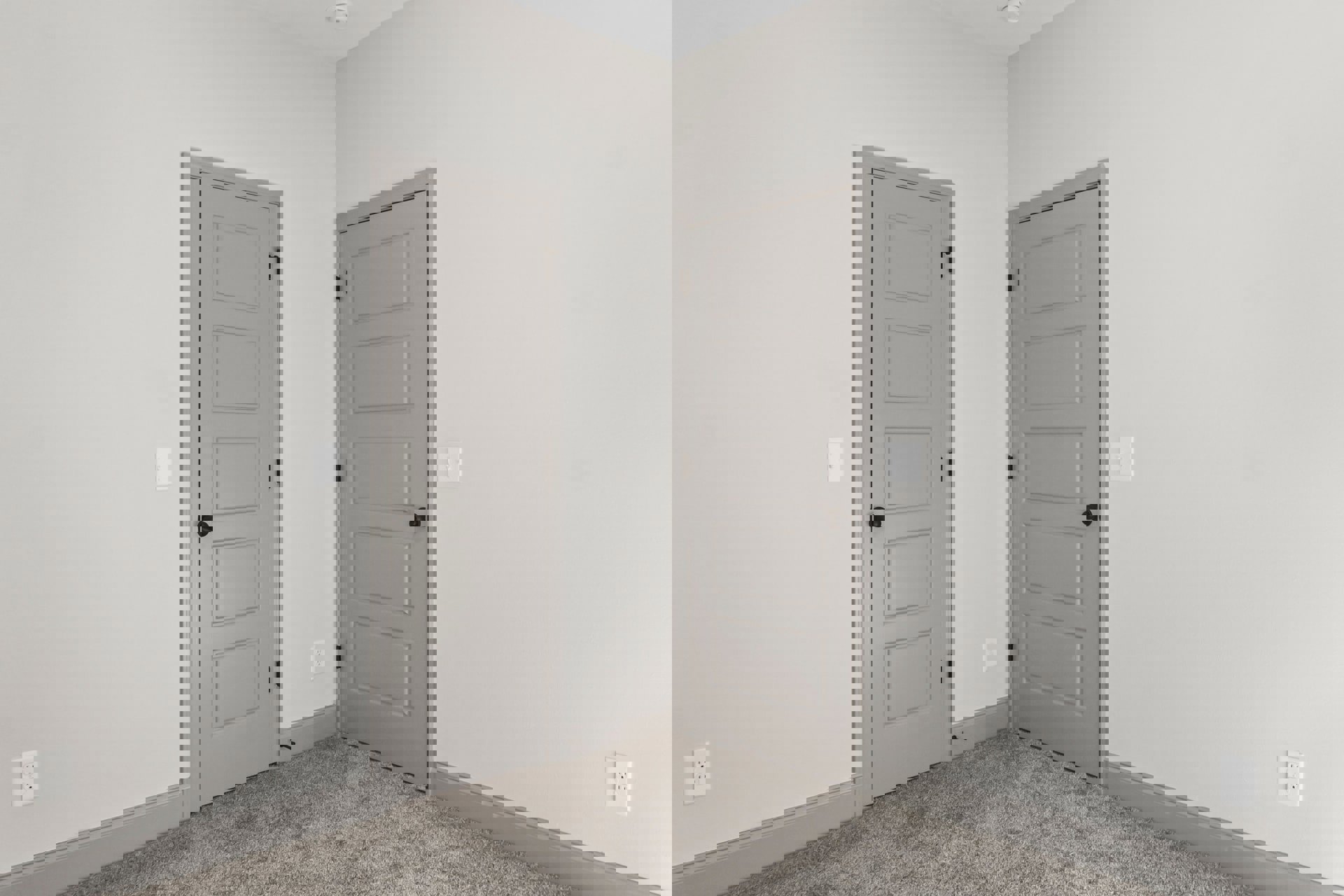 White paneled door with black handle beside a second white door, carpeted floor, white outlet and light switch on plaster wall, smooth ceiling above.