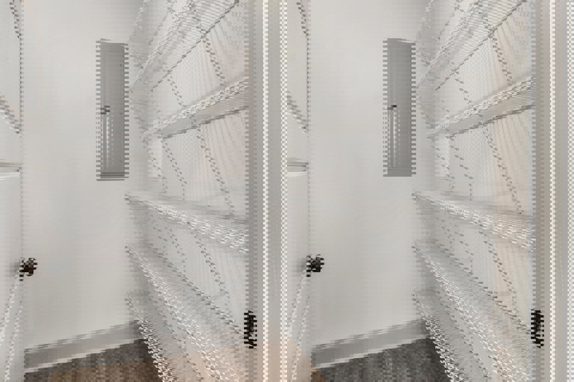 White built-in shelves mounted on a plaster wall beside a white door with a silver handle, metal shelf bars visible, light-colored flooring and ceiling.