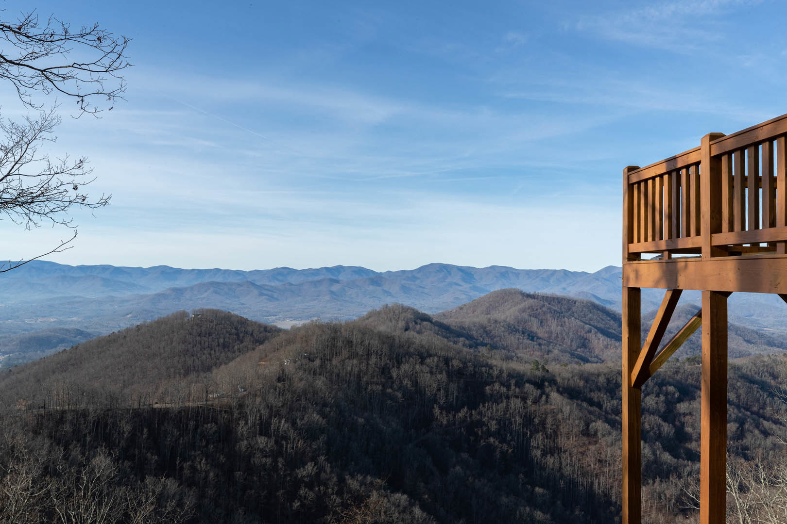 Hickory wood deck with railing, tree branches, and expansive mountain range views under a blue sky with scattered clouds