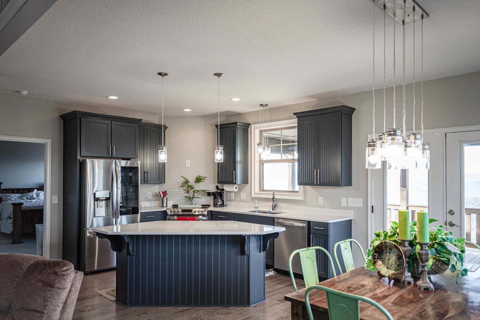 Open kitchen with white cabinetry, central island with seating, wooden dining table, stainless steel refrigerator, blue accent wall, green candlesticks, bowl of leaves, and light