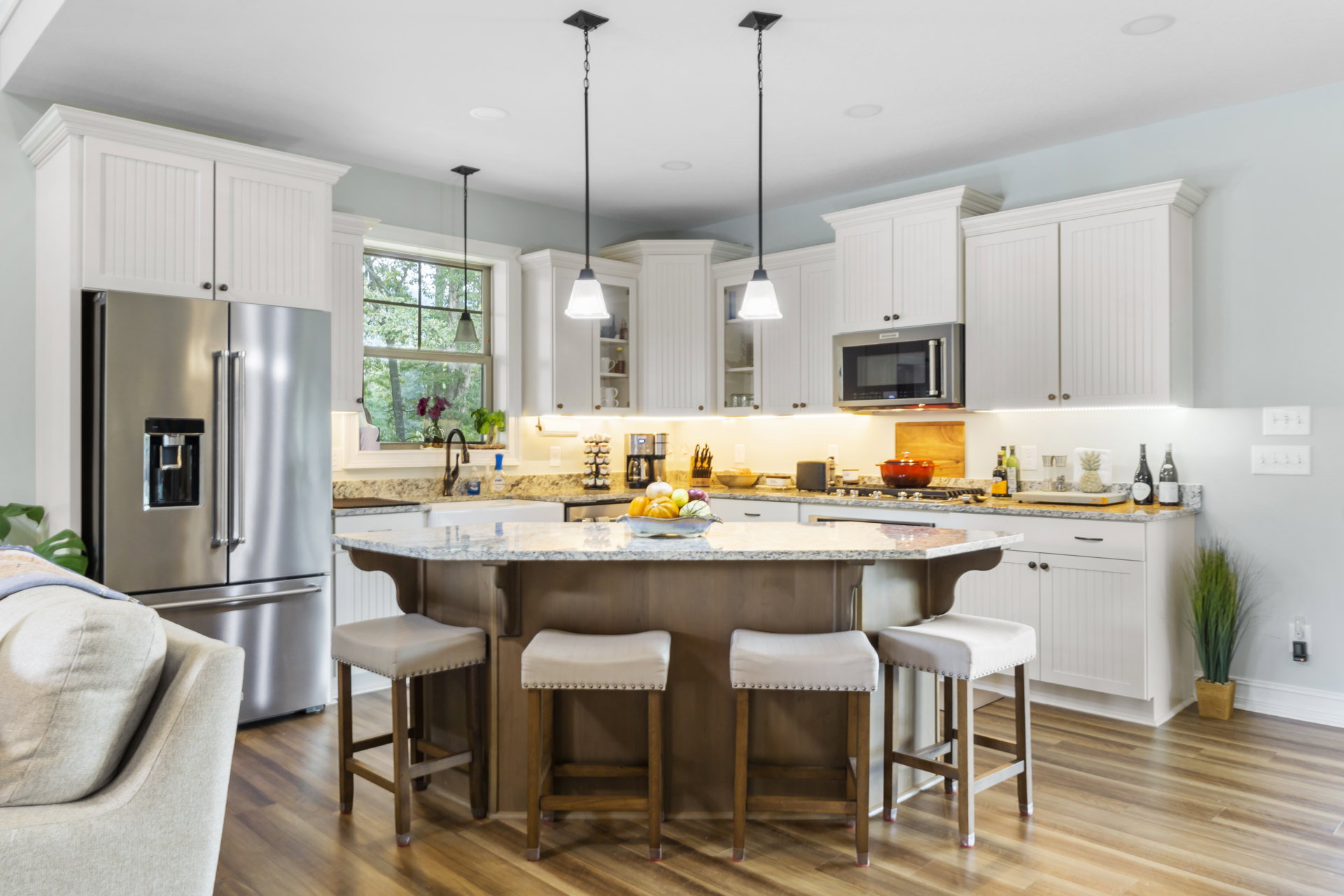 Spacious kitchen featuring a large central island with quartz countertop, two wooden stools, white cabinetry, stainless steel refrigerator, built-in microwave with glass door, and