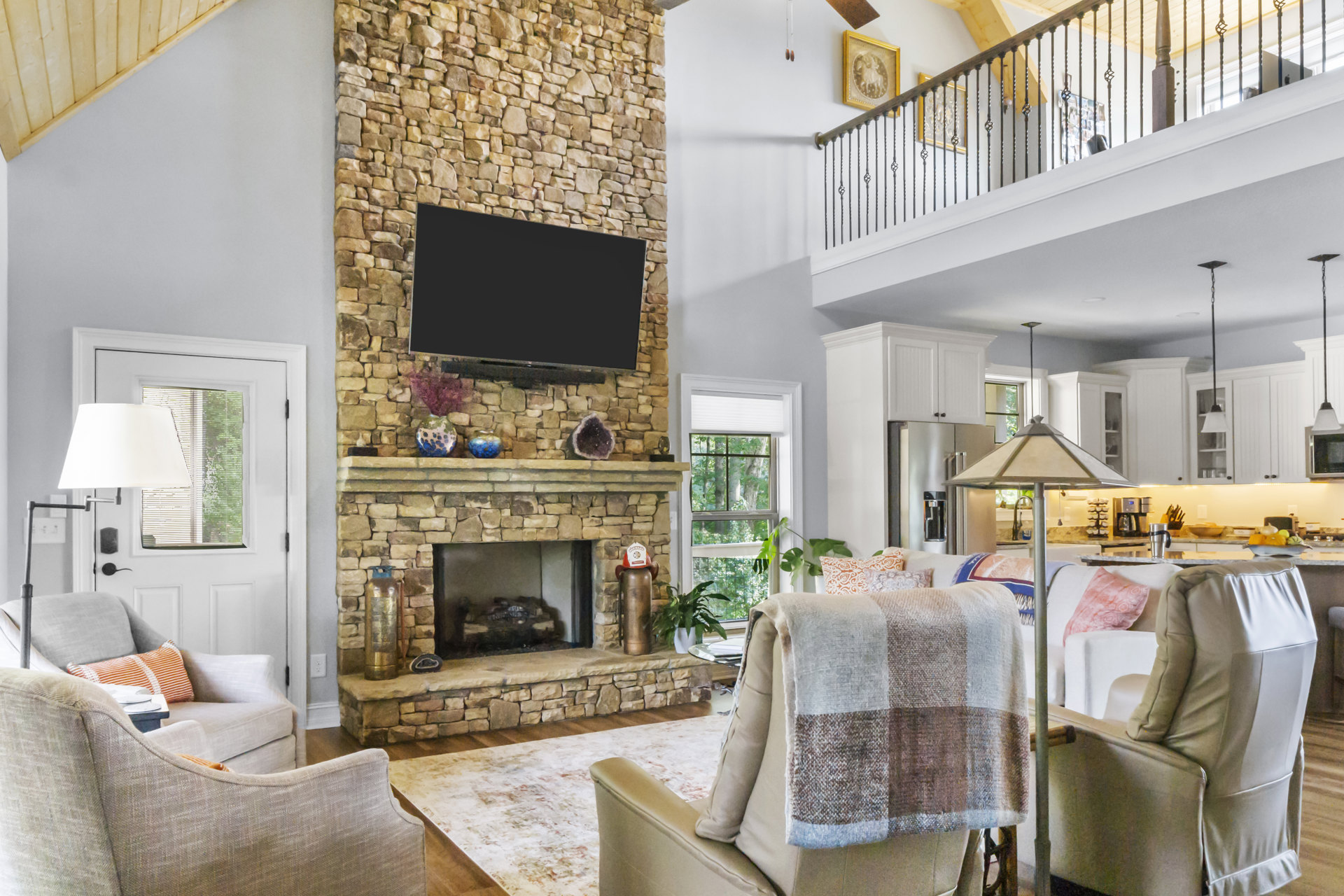 Television mounted above stacked stone fireplace, gray sectional sofa with throw blanket and pillow, wood coffee table, neutral walls, cozy living room setting
