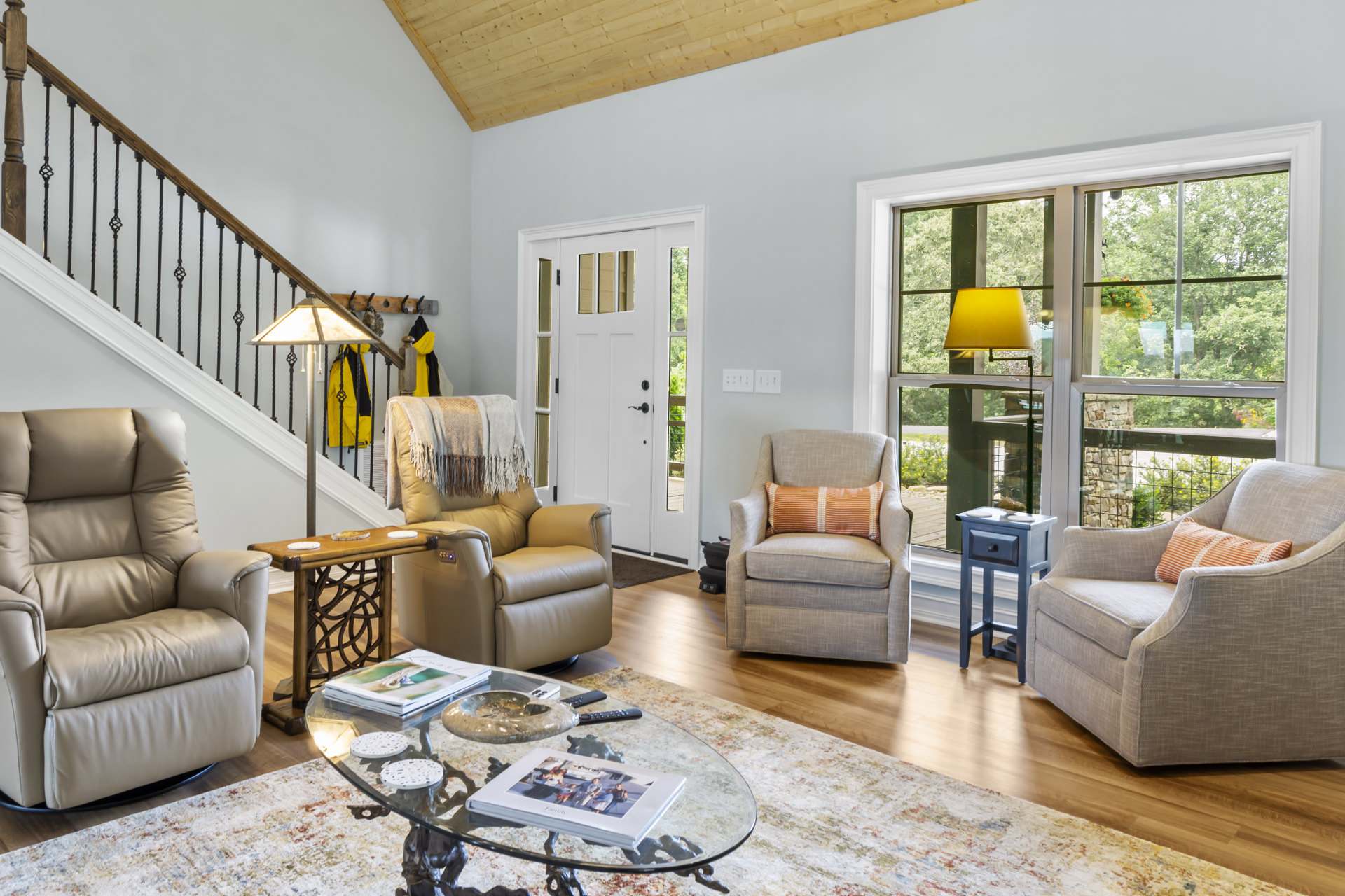 Living room with white leather recliner and tan recliner chair draped with a blanket, glass coffee table, chairs with pillows, family photo book, neutral walls and flooring