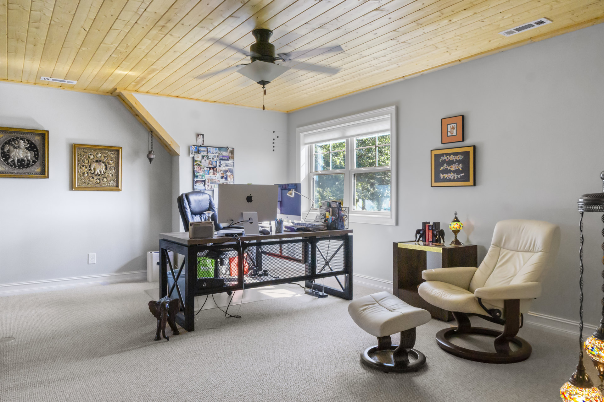 Modern study with a wooden desk, white chair, wire mesh desk organizer, framed elephant artwork, and ceiling fan above light hardwood floors