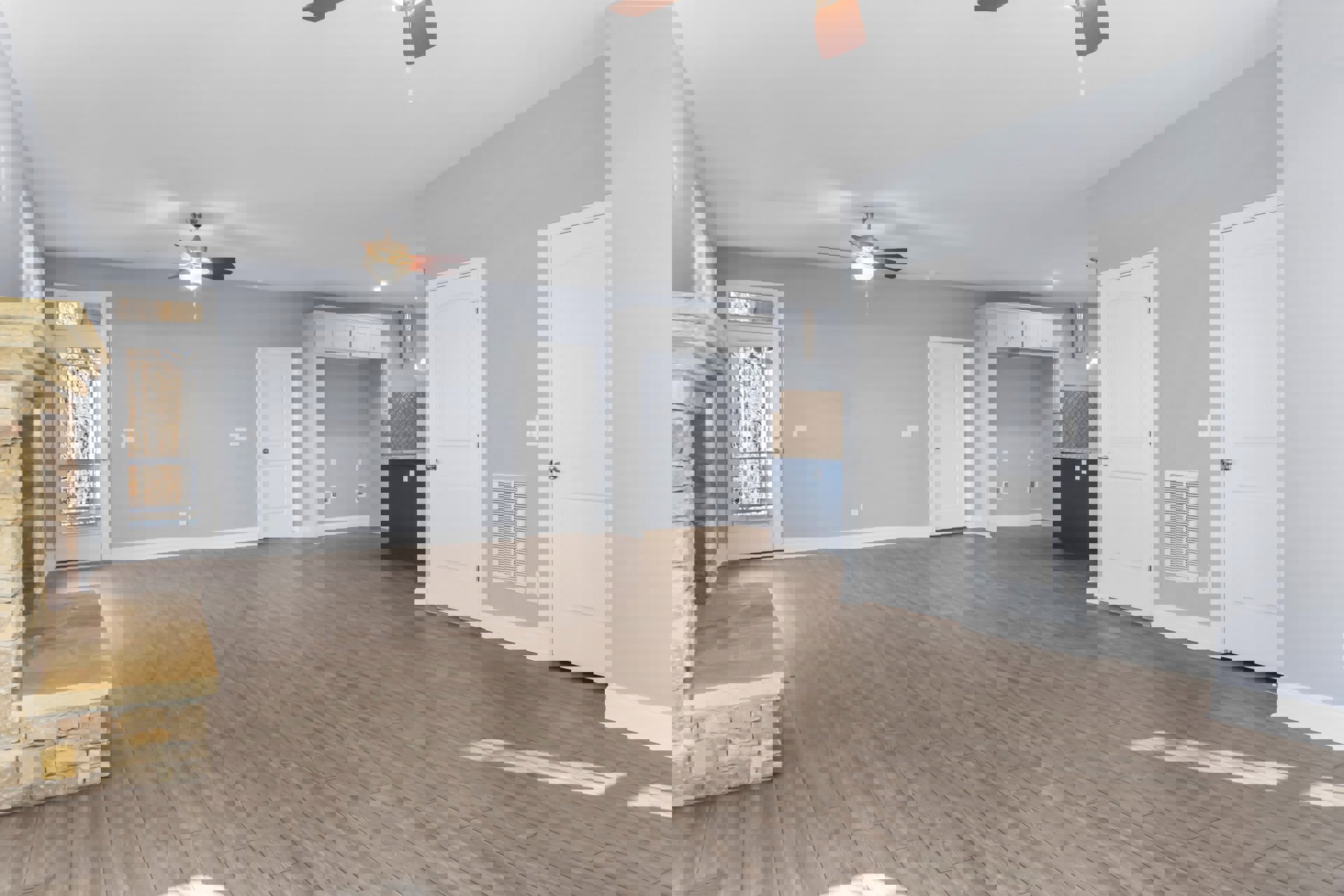 Wood flooring with white baseboards, ceiling fan with light fixture, white door featuring silver knob and window, neutral walls, natural light illuminating interior space.