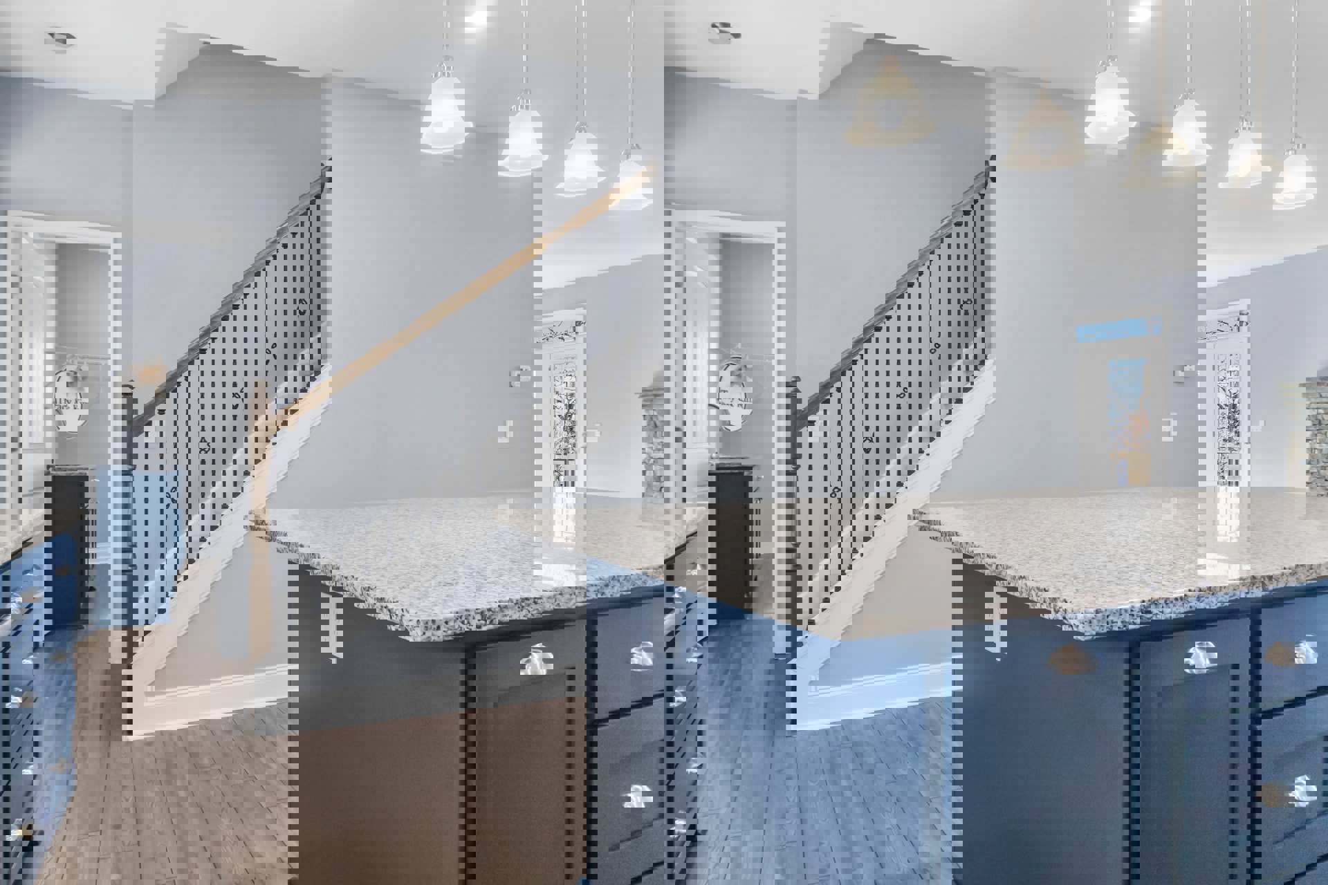 Marble kitchen island with blue cabinetry, integrated sink, and modern light fixture, adjacent to staircase and hardwood flooring