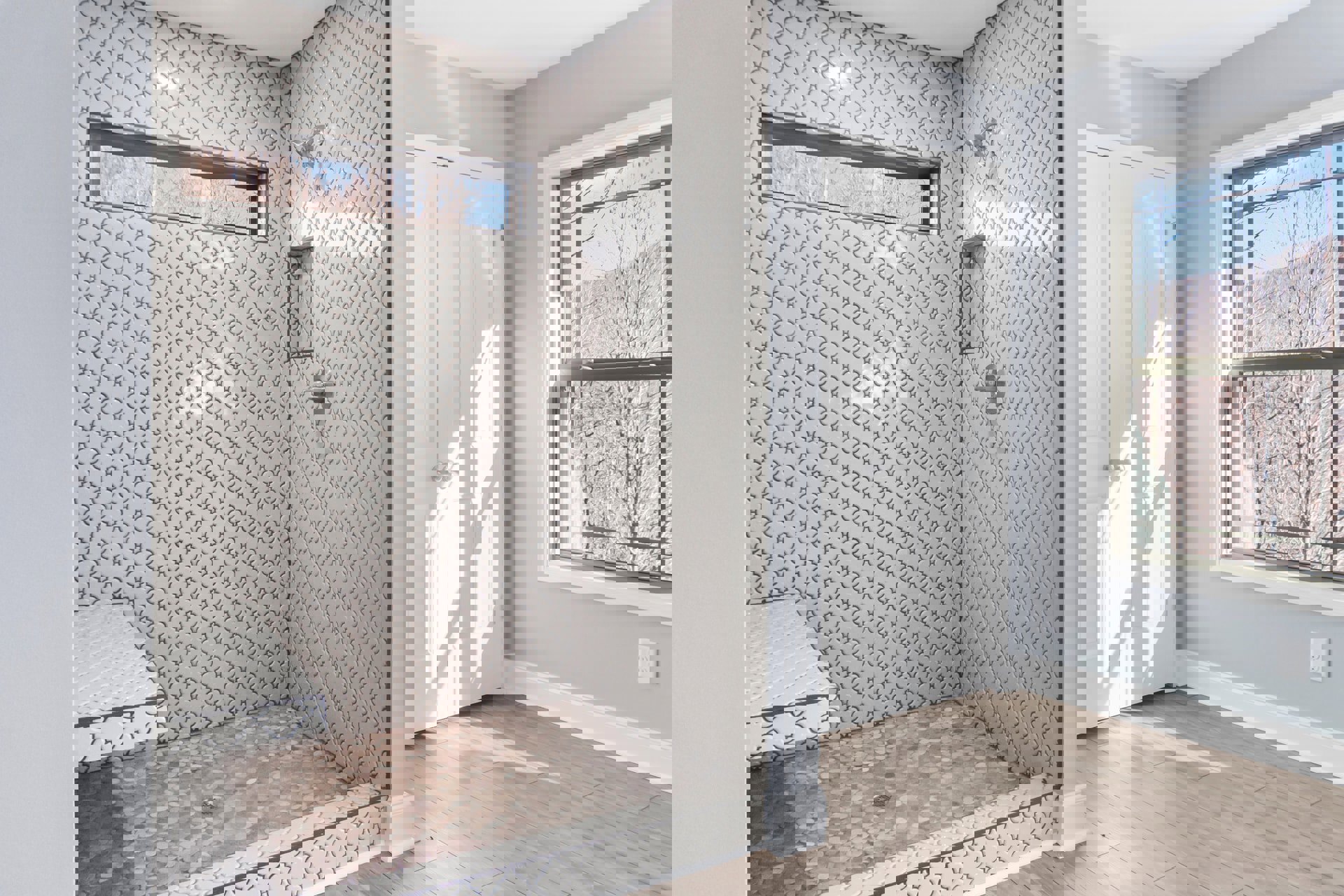 Bathroom with glass shower enclosure, window overlooking trees, white and brown tile shower floor, white door with silver handle, plaster walls, and ceiling.