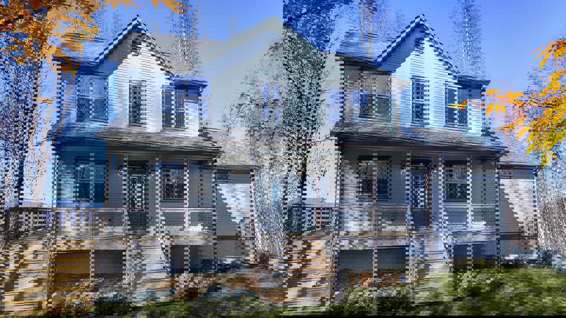 White siding house with covered front porch, wooden stairs, glass windows reflecting nearby trees, and paneled front door