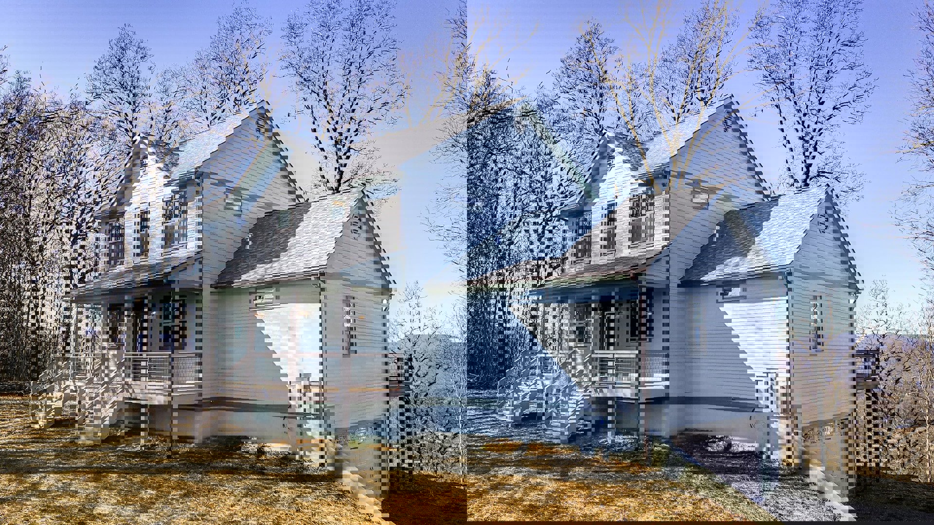 White siding house with covered front porch, large windows, shingled roof, landscaped yard with green grass, mature tree, and blue sky in background