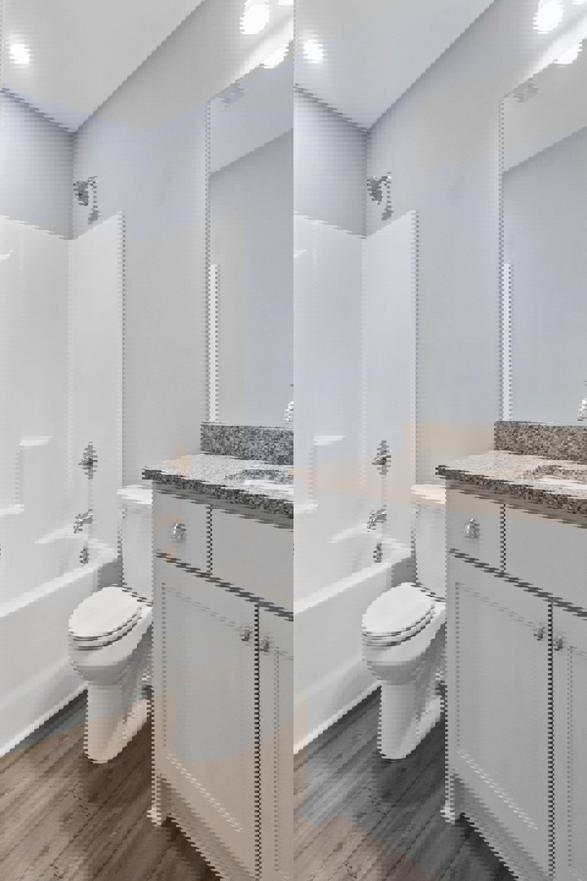 White bathroom with ceramic tile floor, modern vanity with silver handles, undermount sink, chrome faucet, and toilet adjacent to a tiled tub and shower.