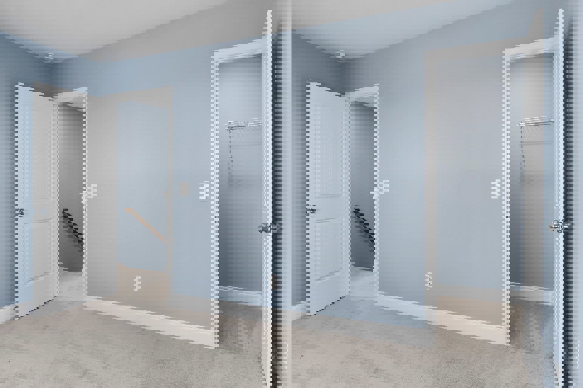 Carpeted bedroom with blue walls, white trim, open white door with silver knob, visible closet, and wall-mounted handrail