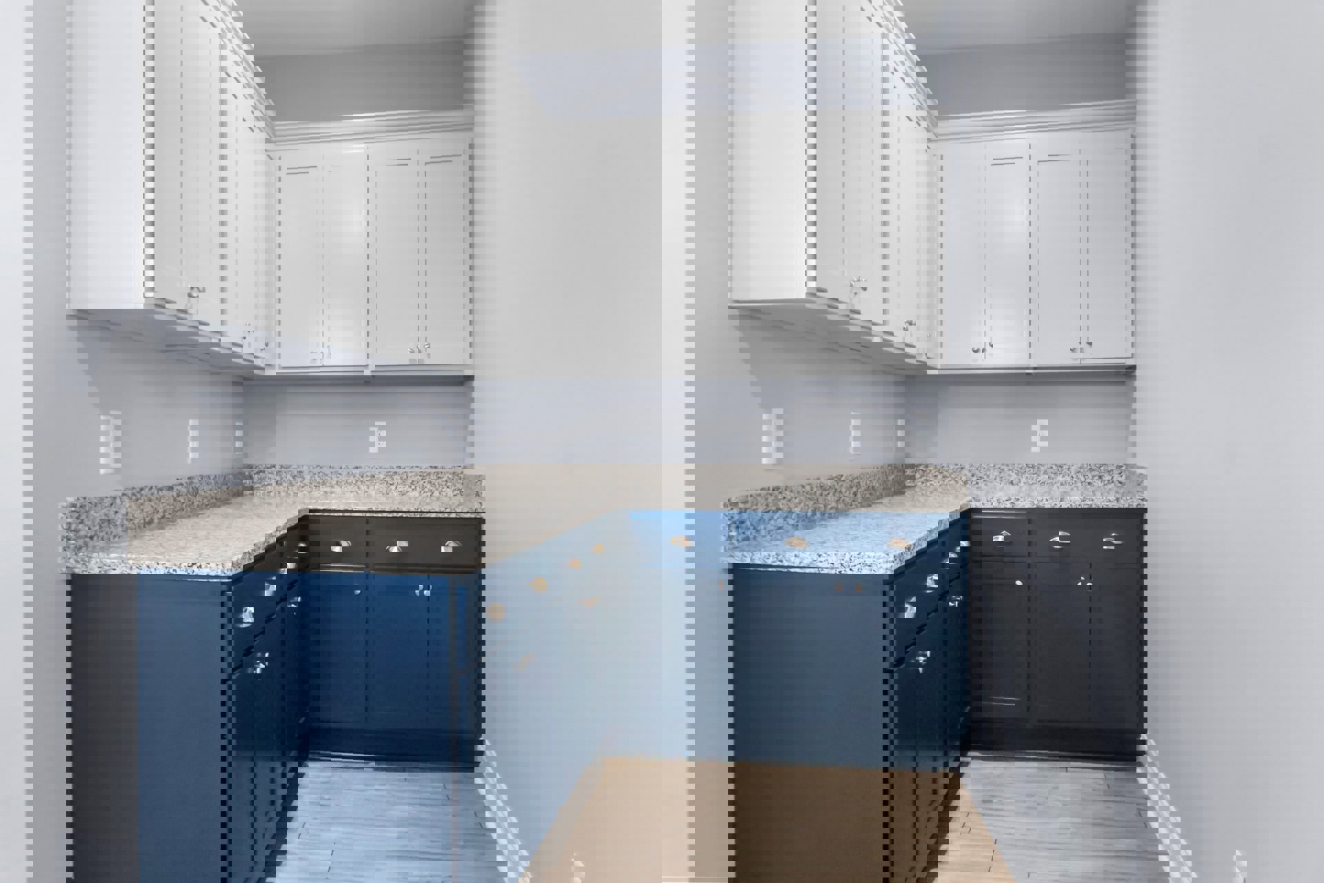 Kitchen with blue and white cabinets, marble countertops, wood flooring with black border, stainless steel appliances, and a person holding a blue object near the sink.