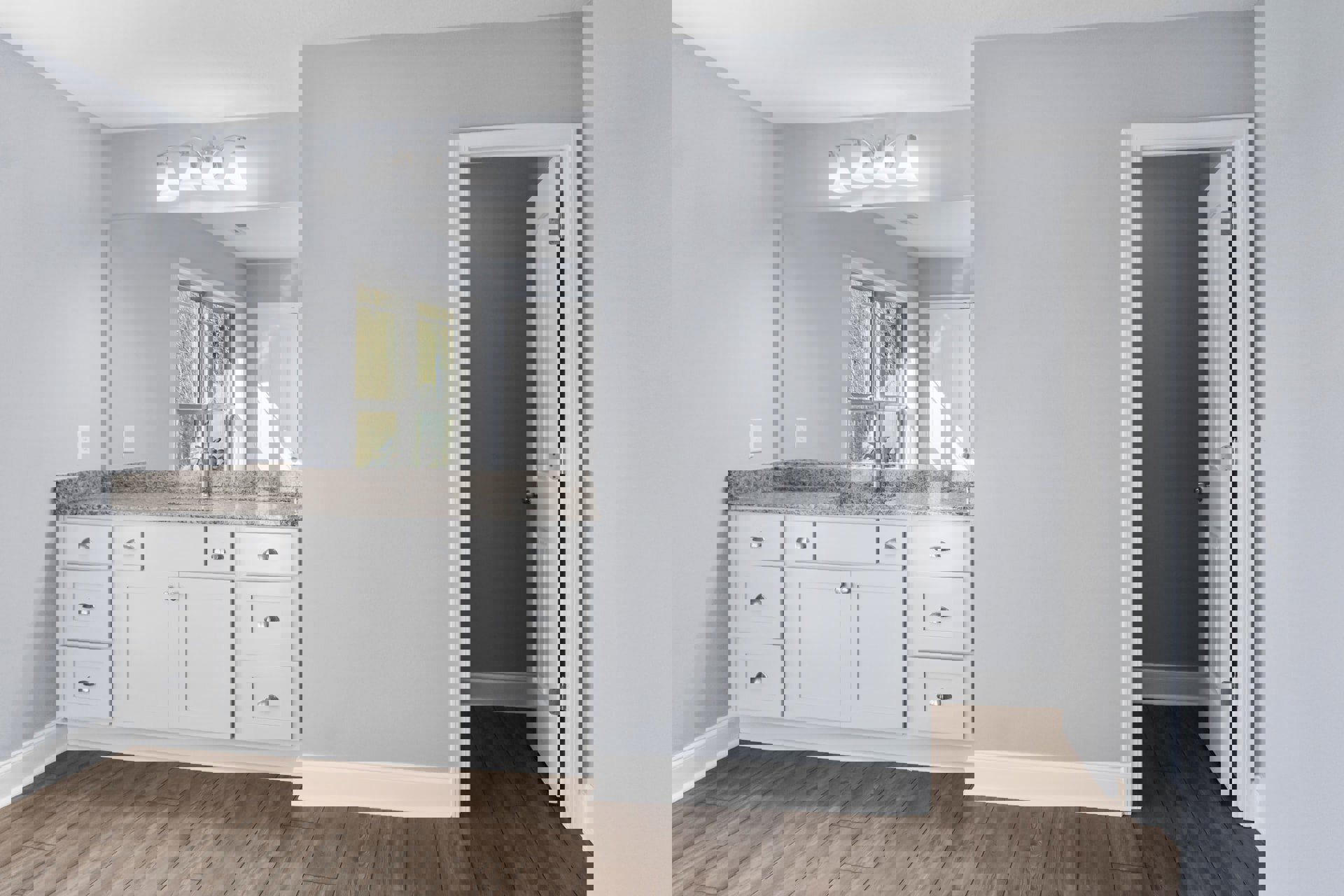 Bathroom with a white sink set in a kitchen-style countertop, wood flooring, white cabinetry with drawers, grey wall, white door, window, and a two-lamp light fixture.