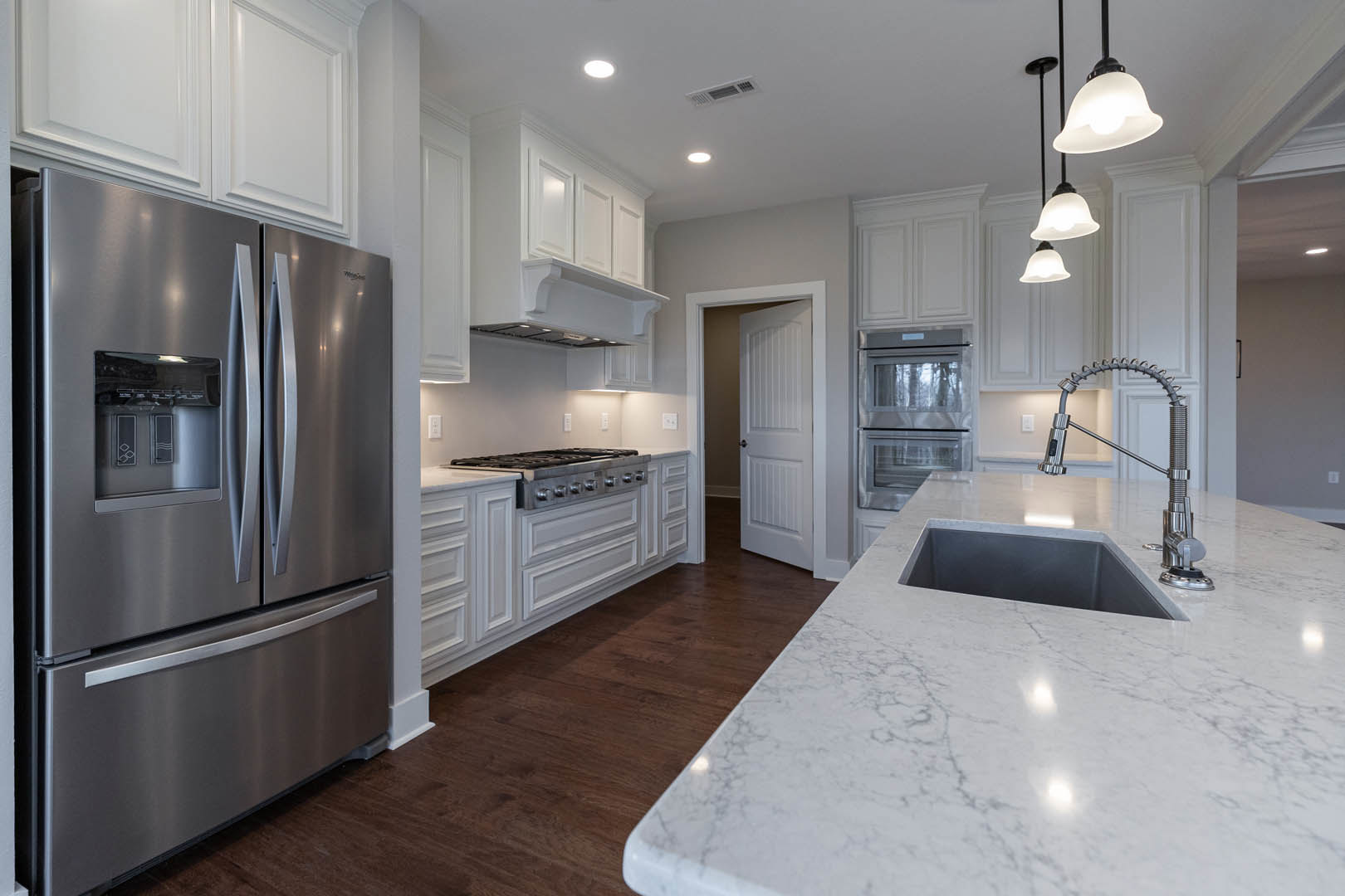 White kitchen with shaker cabinets, stainless steel refrigerator, marble countertop with undermount sink, chrome faucet, and stainless steel oven