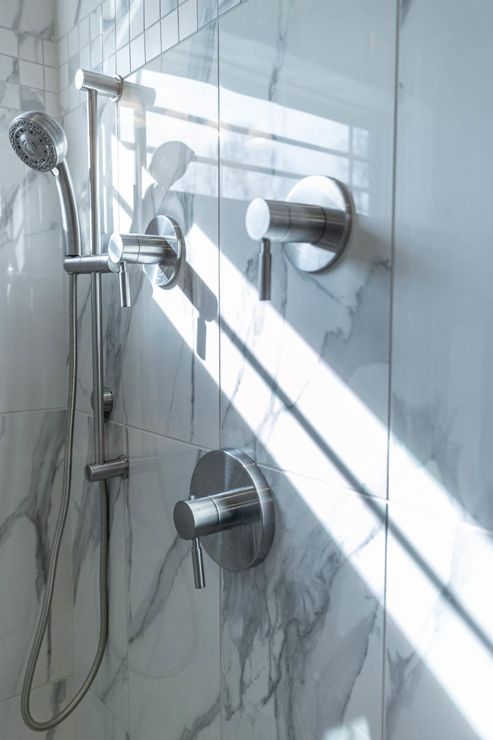 Chrome shower head and matching faucets mounted on light tiled bathroom wall