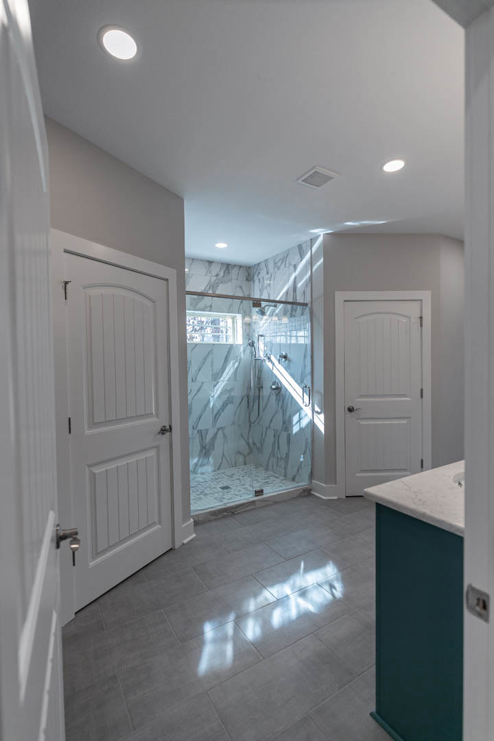 Bathroom featuring a marble-tiled shower, white paneled doors with contrasting handles, and light reflecting off polished flooring