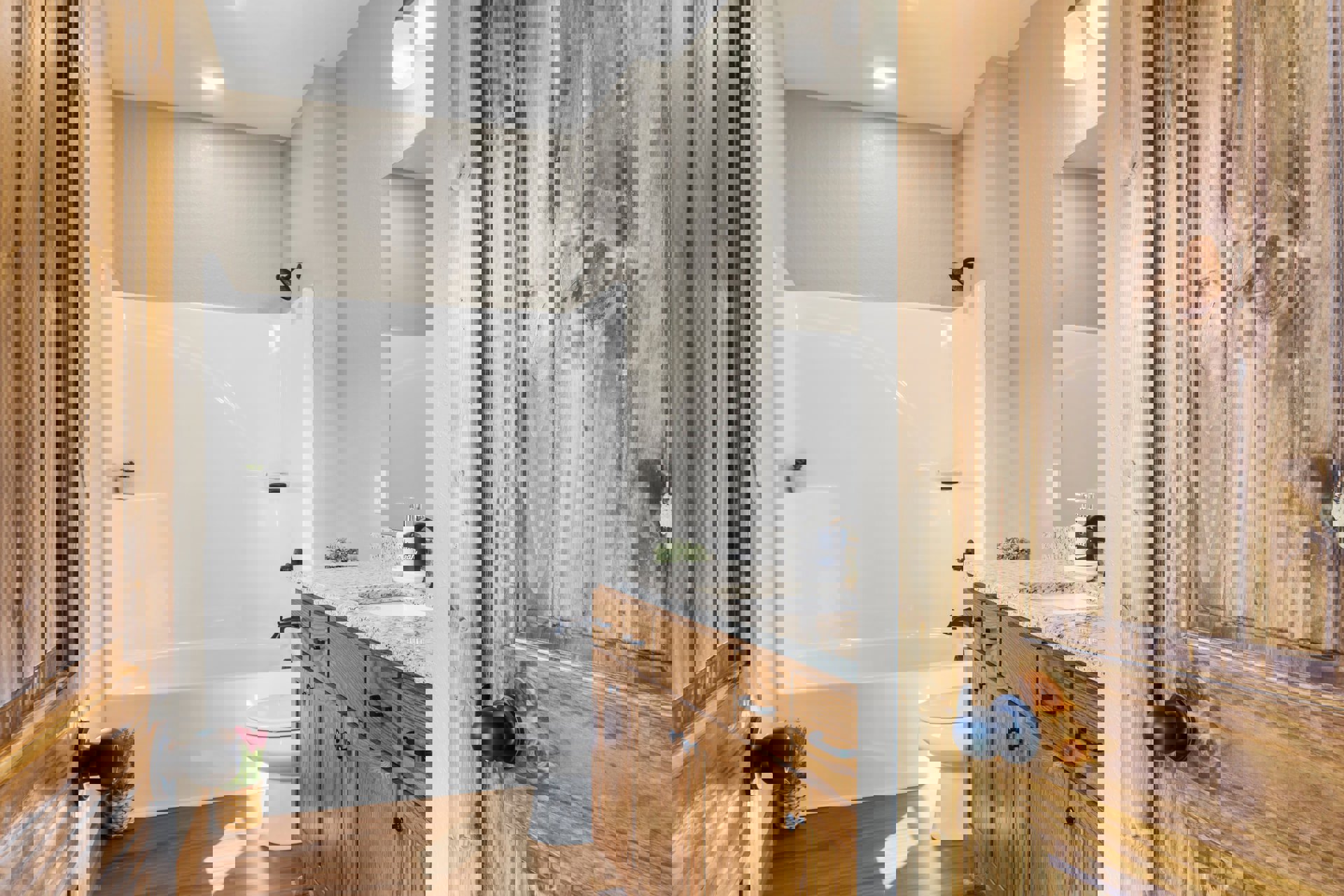 White freestanding bathtub beside a wooden door, white sink, tiled walls, wood flooring, black door knob, and chrome shower head in a modern bathroom.