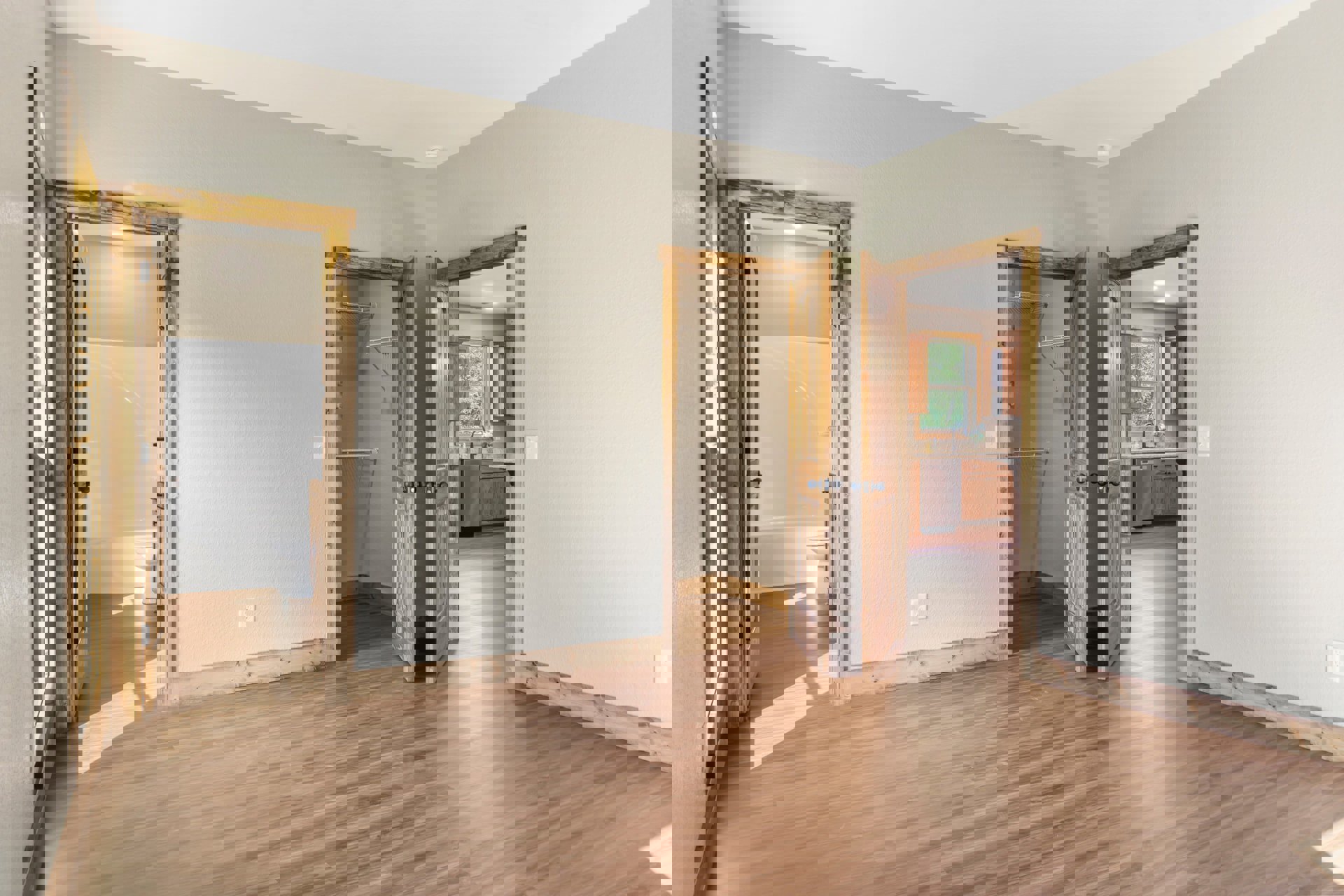 Wood floor room featuring two open doors, silver refrigerator, white bathtub, sink, toilet, closet with shelf, and window overlooking trees.