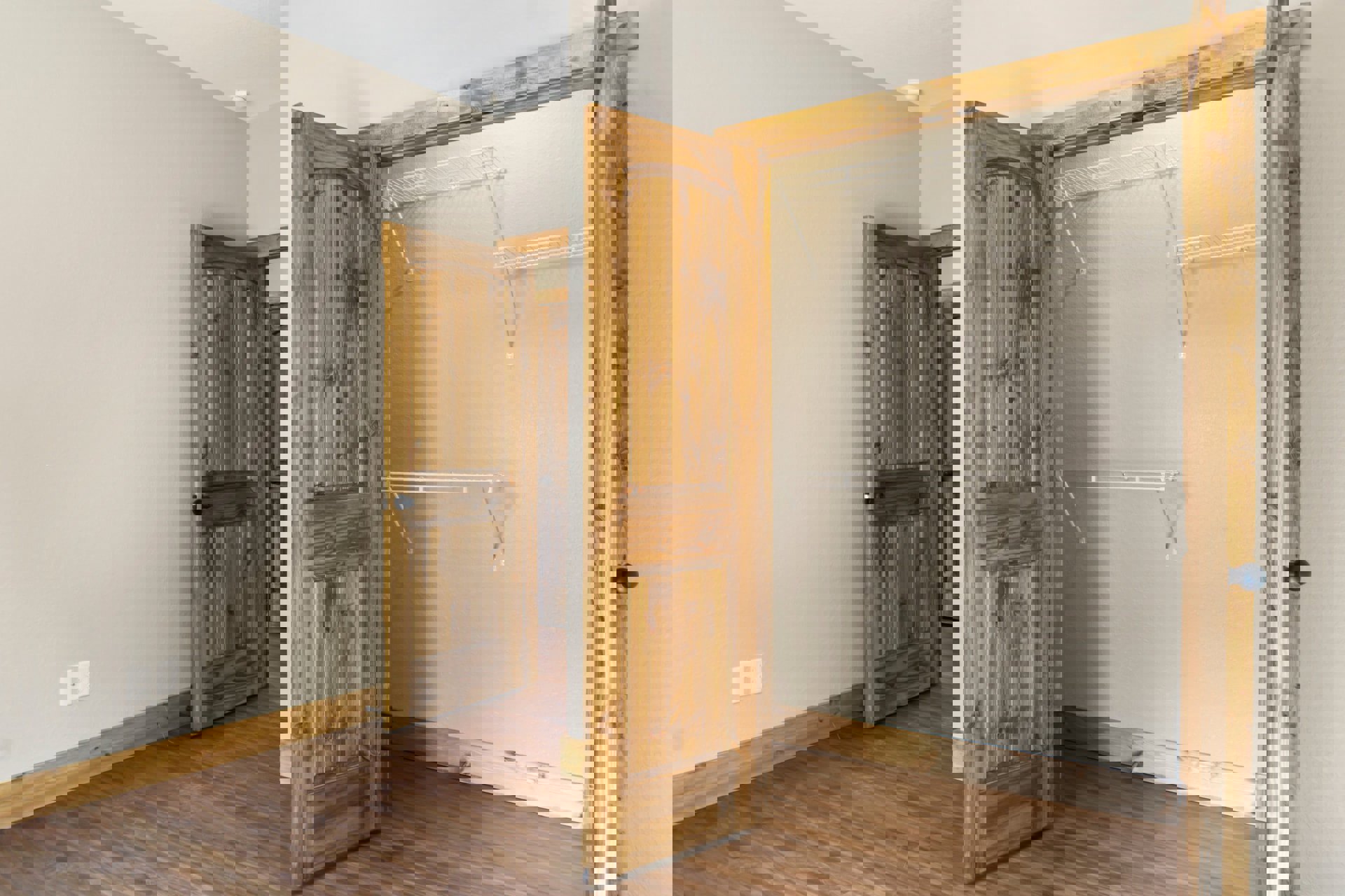 Walk-in closet with two wood doors, one open to reveal hardwood flooring and plaster walls, featuring modern door handles