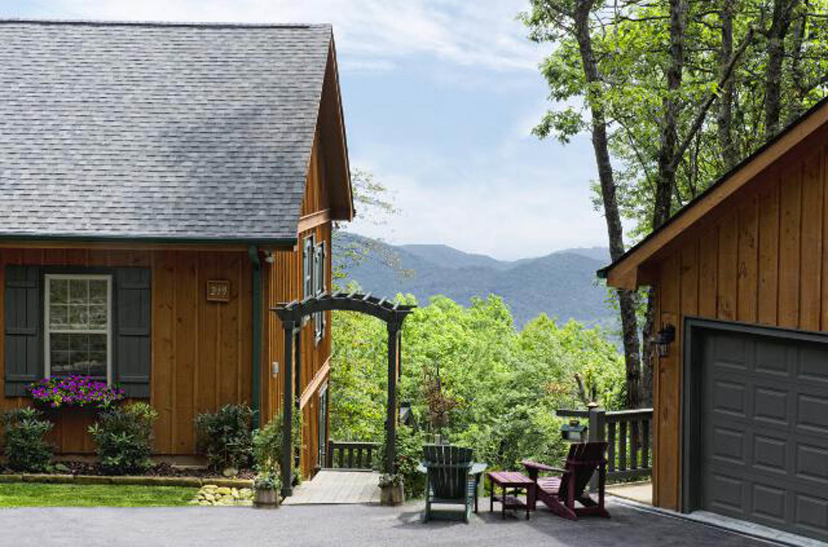 Modern home with black front door, white-framed windows, spacious porch, potted plants, and mountain views in the background