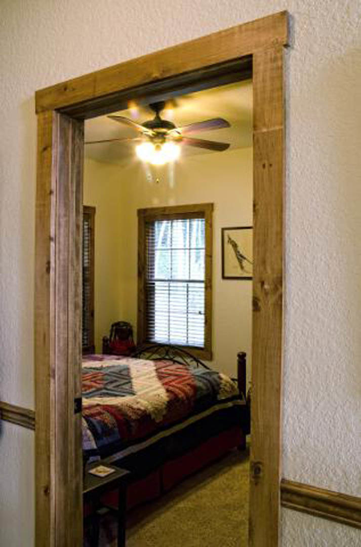 Bedroom with a wall-mounted mirror, bed featuring a quilt and pillows, window with white blinds, ceiling fan overhead, neutral color palette