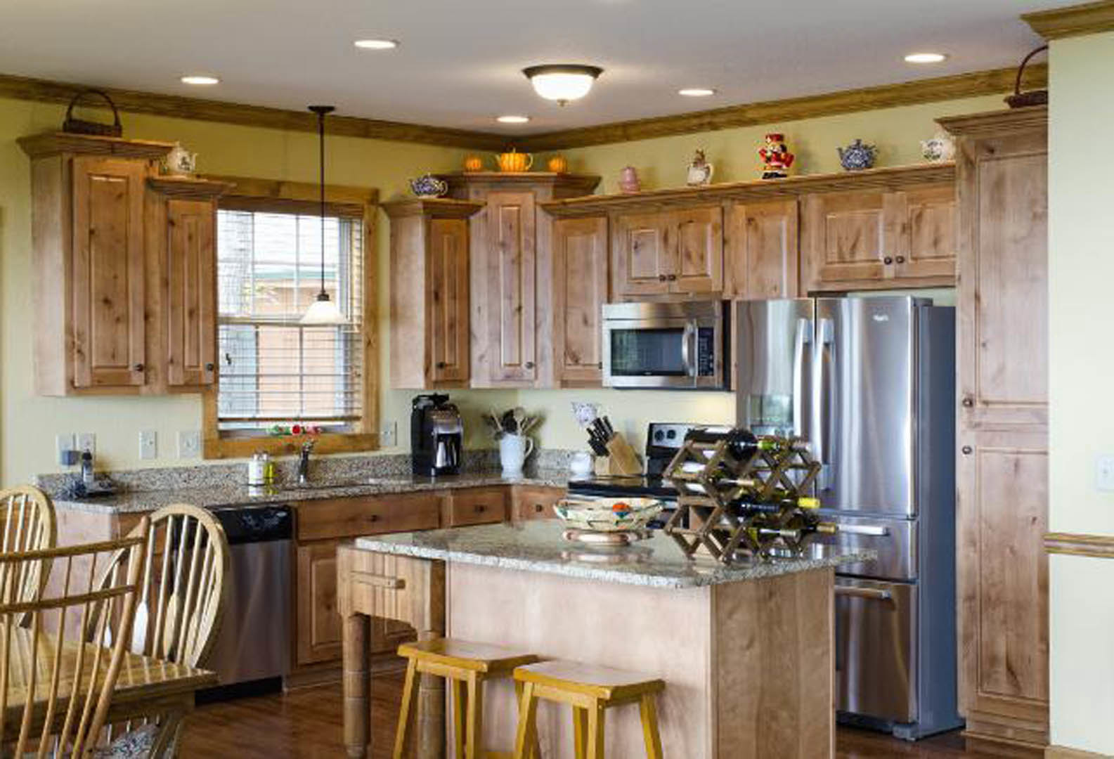 Kitchen with stainless steel refrigerator, built-in wine rack on countertop, bar area with stools, white table surface, wood cabinetry, and modern appliances