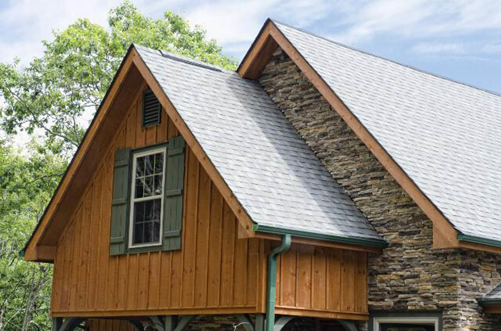 Stone exterior wall with white-framed window and dark roof, surrounded by trees and sky