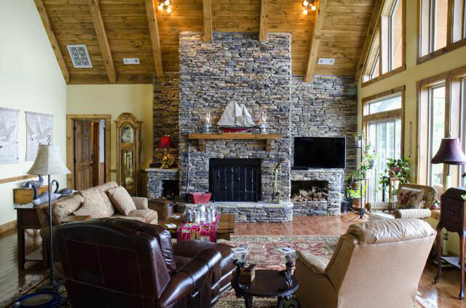 Living room featuring a stone fireplace, gray upholstered couch, leather accent chair, round coffee table with metal base, hardwood floors, and black-framed door with metal bars