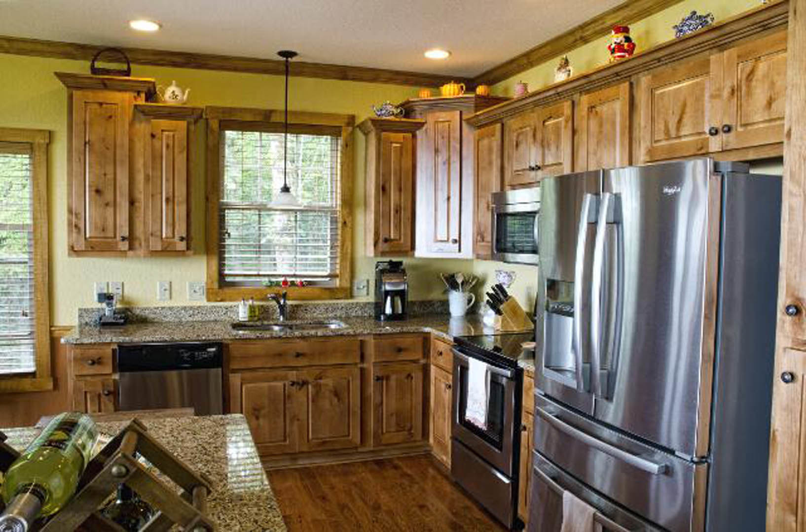 Wooden kitchen cabinets with stainless steel refrigerator, stove, and microwave, light countertops, and a blurred chair in the foreground