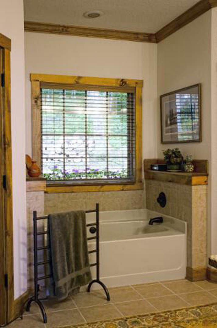 White-tiled bathroom featuring a freestanding bathtub beneath a window with horizontal blinds, towel hanging on a metal rack, and potted plant on the windowsill