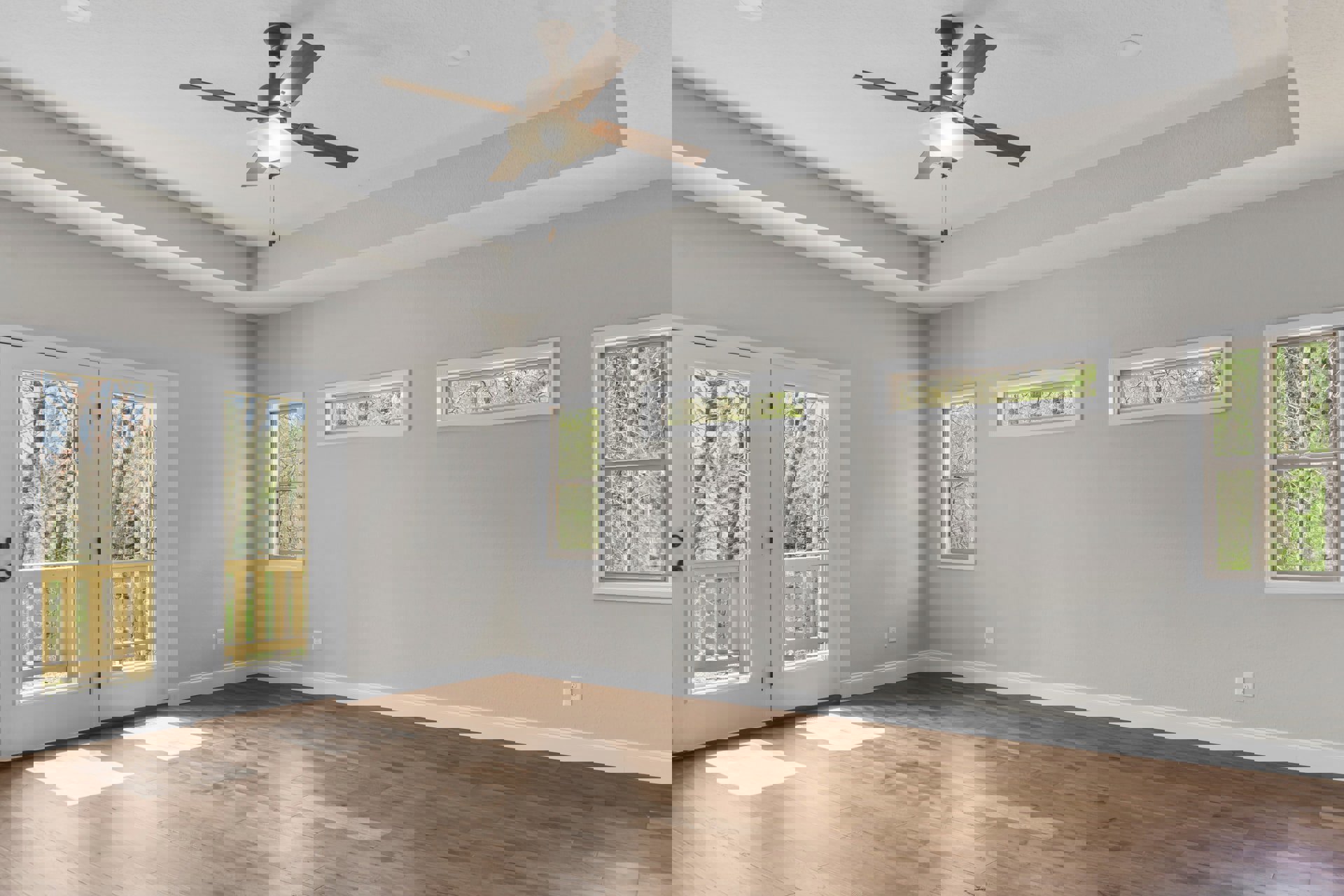 Ceiling fan with light fixture, white plaster walls, wood flooring, large windows with white frames showing trees outside, double glass doors