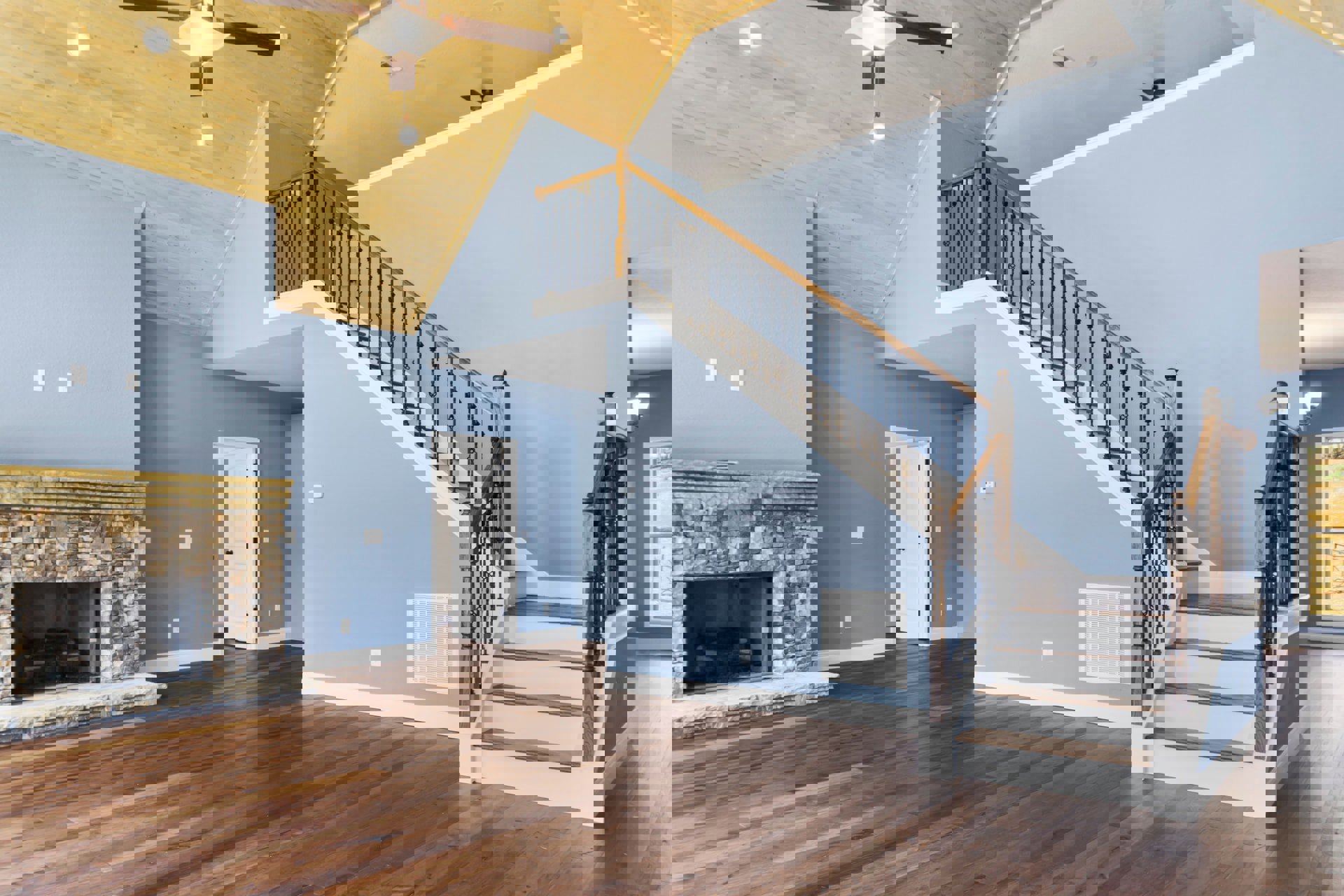 Hardwood floor living area featuring a stone surround fireplace, blue accent wall with white vent, white door with black knobs, and staircase with wood railing