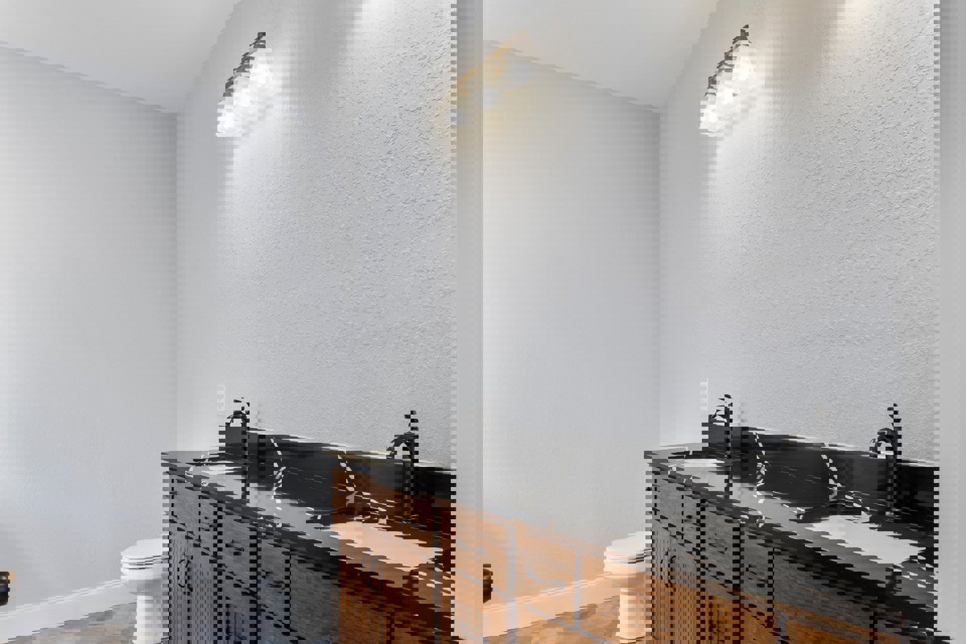 Bathroom with black stone countertop featuring white veining, wooden cabinets, white toilet, four-light fixture above mirror, and white walls.