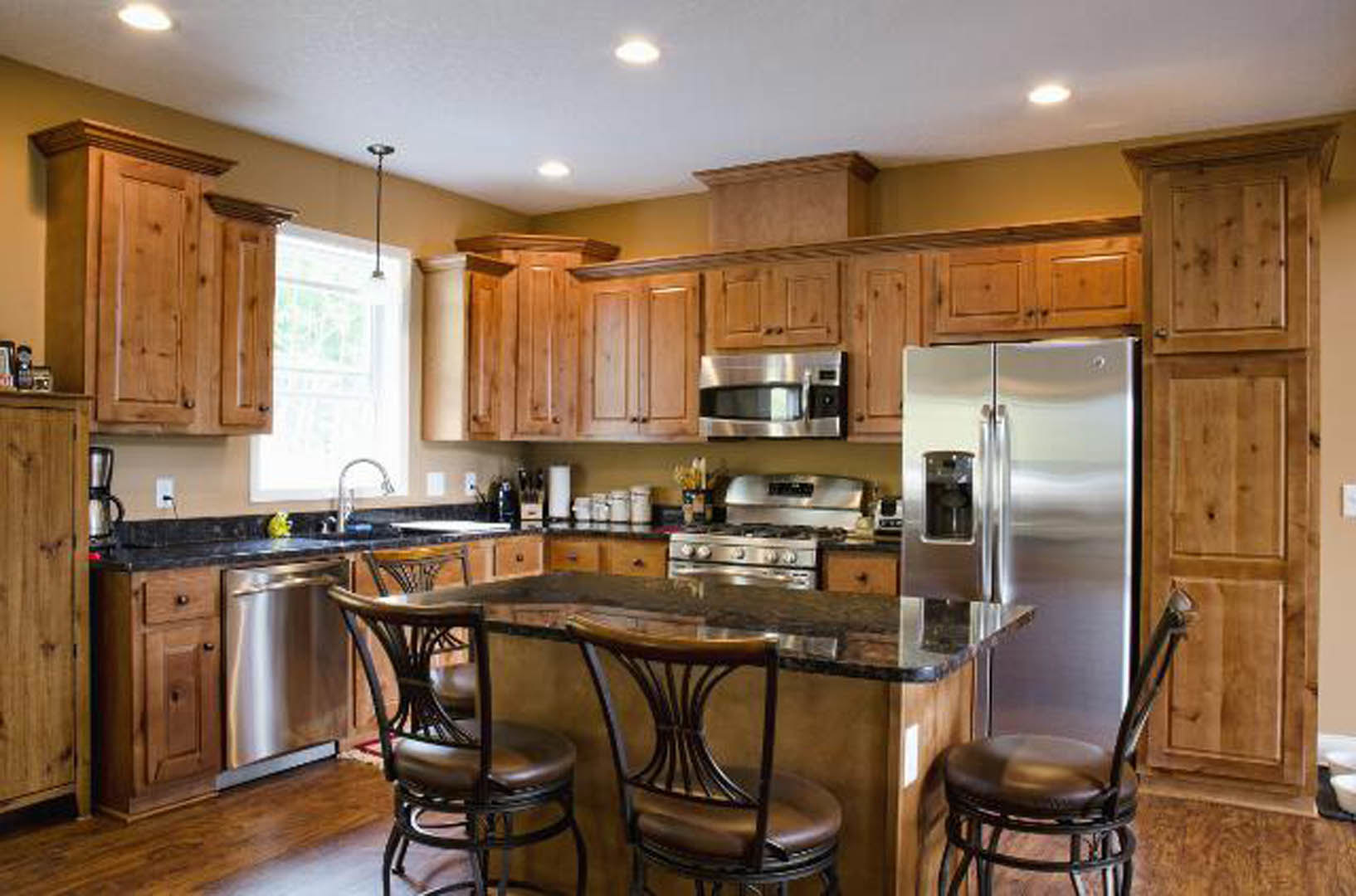 Spacious kitchen featuring a large quartz island with barstools, stainless steel refrigerator and oven, white shaker cabinets, and pendant lighting